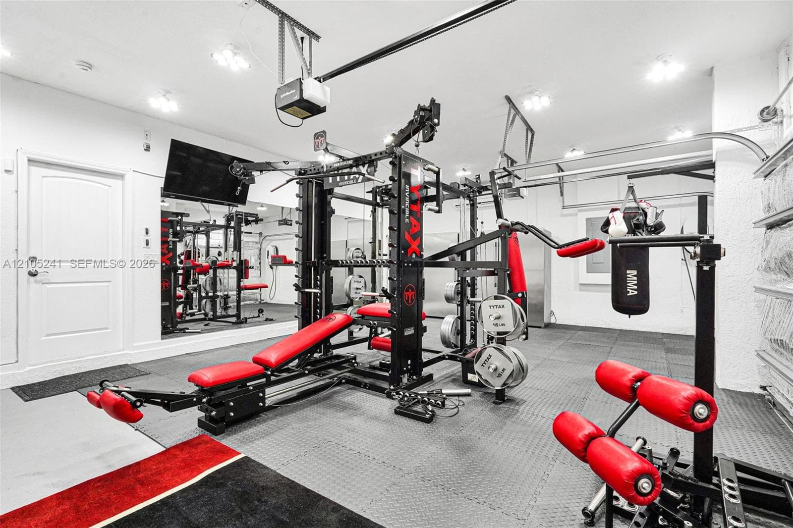 Dedicated workout area featuring rubber flooring, recessed lighting, expansive wall-mounted mirrors, and an interior door