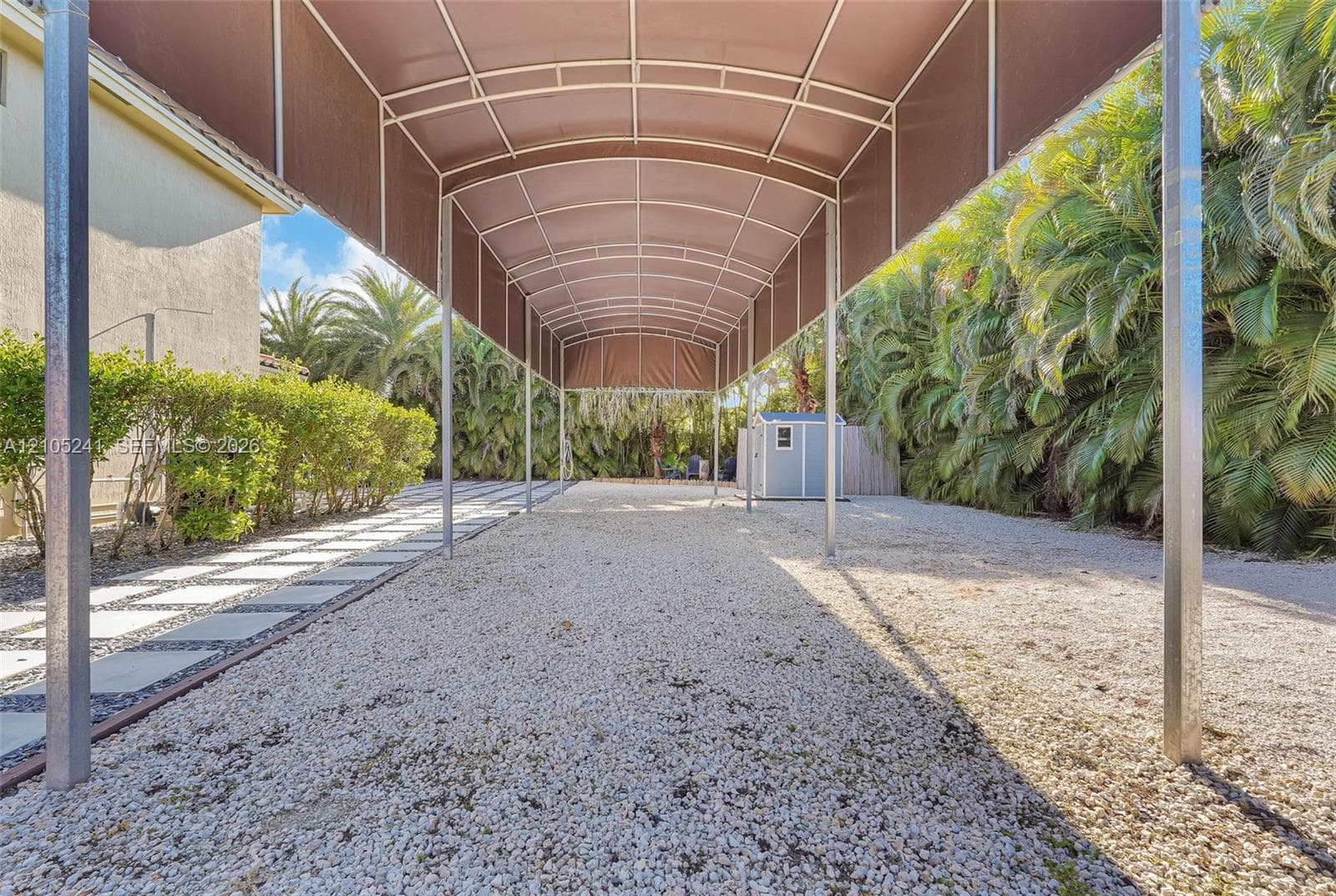 Expansive covered gravel driveway with a metal frame and brown fabric canopy
