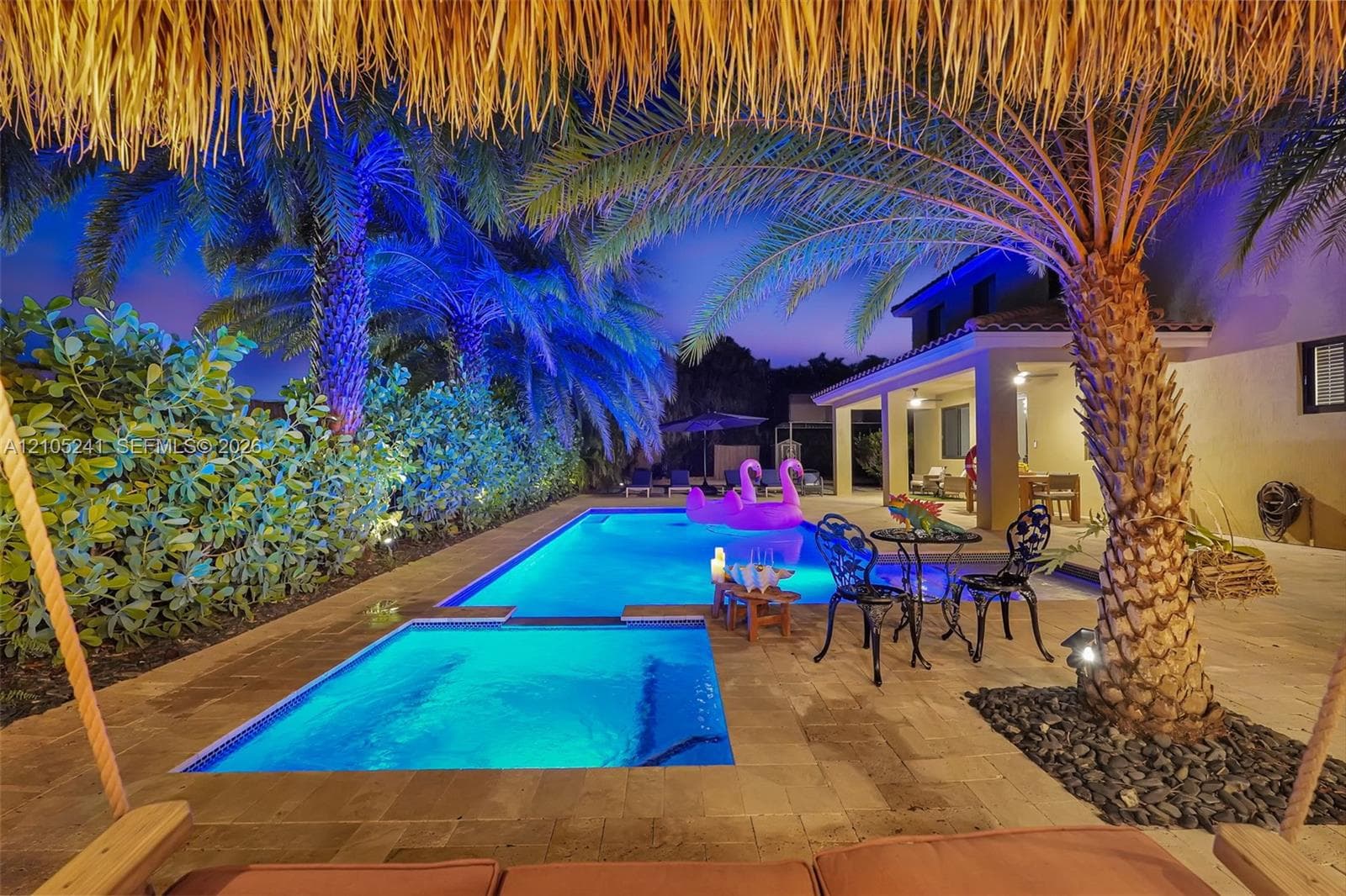 Swimming pool with integrated spa, paver patio, mature palm trees, and covered outdoor living space