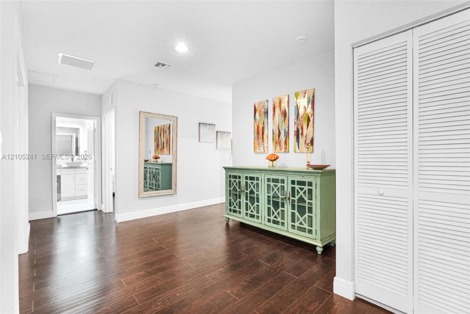 Rich wood-finish flooring, recessed lighting, white louvered bifold doors, and a neutral wall color