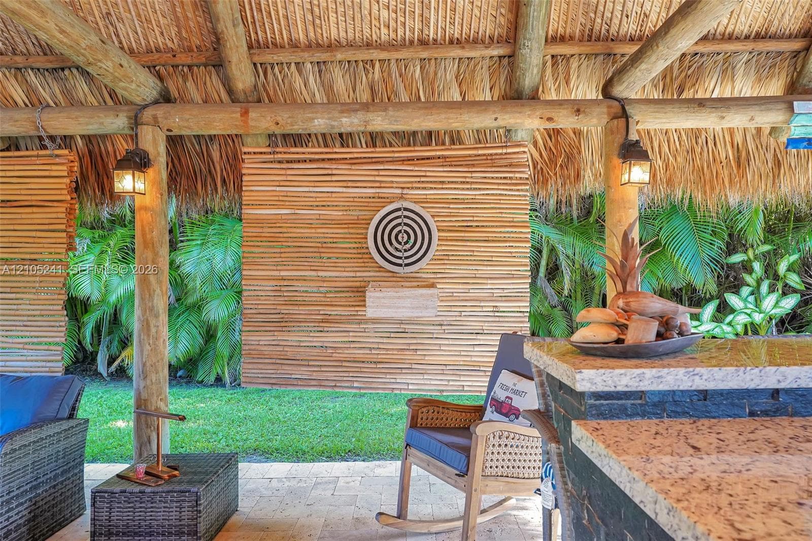 Thatch-roofed outdoor structure featuring exposed wood beams, a stone-clad bar with a light-toned countertop, and integrated lighting fixtures