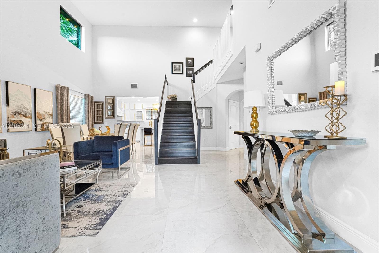 Soaring ceilings, expansive white tile flooring, and a contemporary staircase with dark wood treads