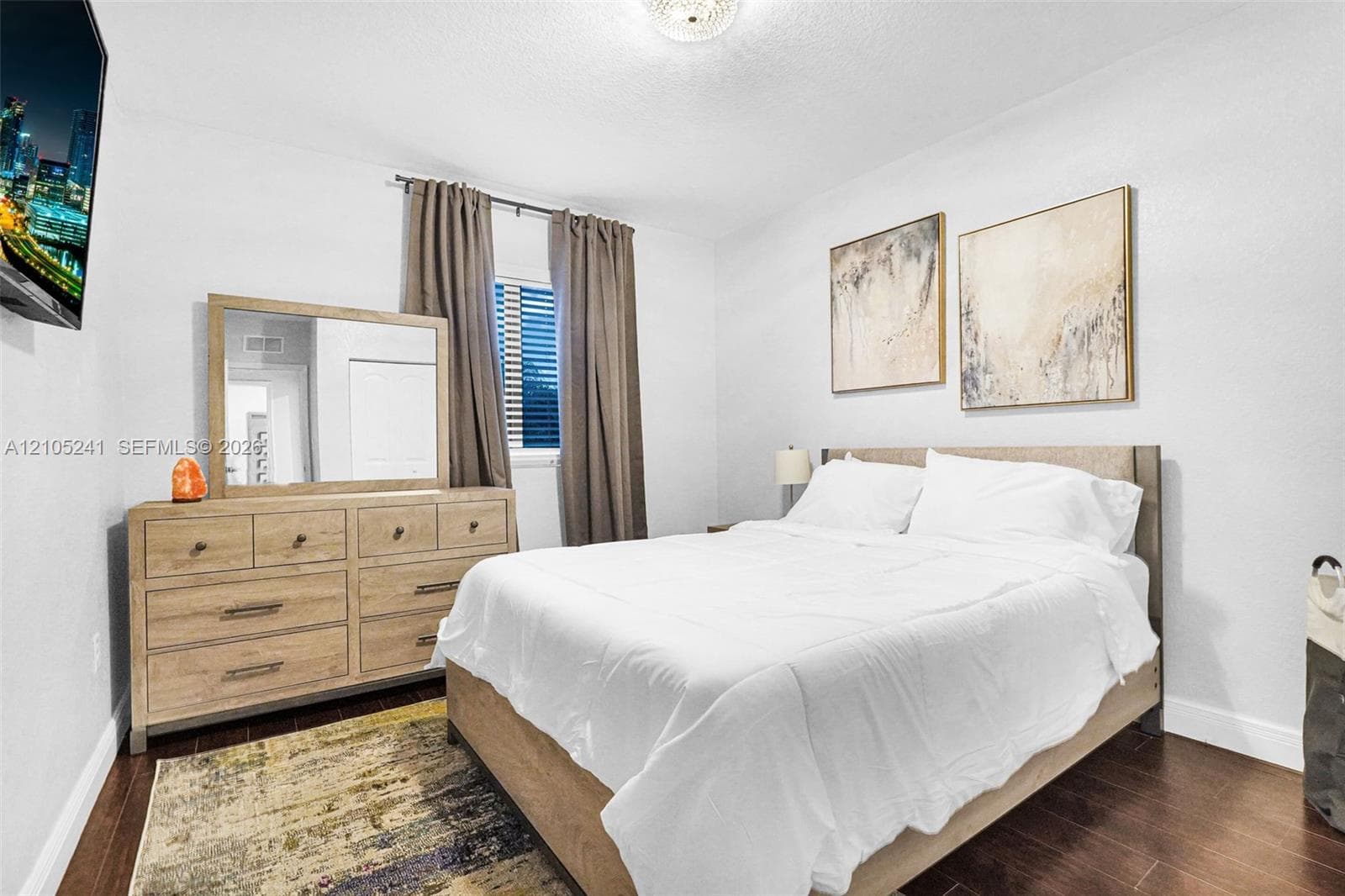 Rich wood-finish flooring, white painted walls, window with horizontal blinds, and a ceiling-mounted light fixture
