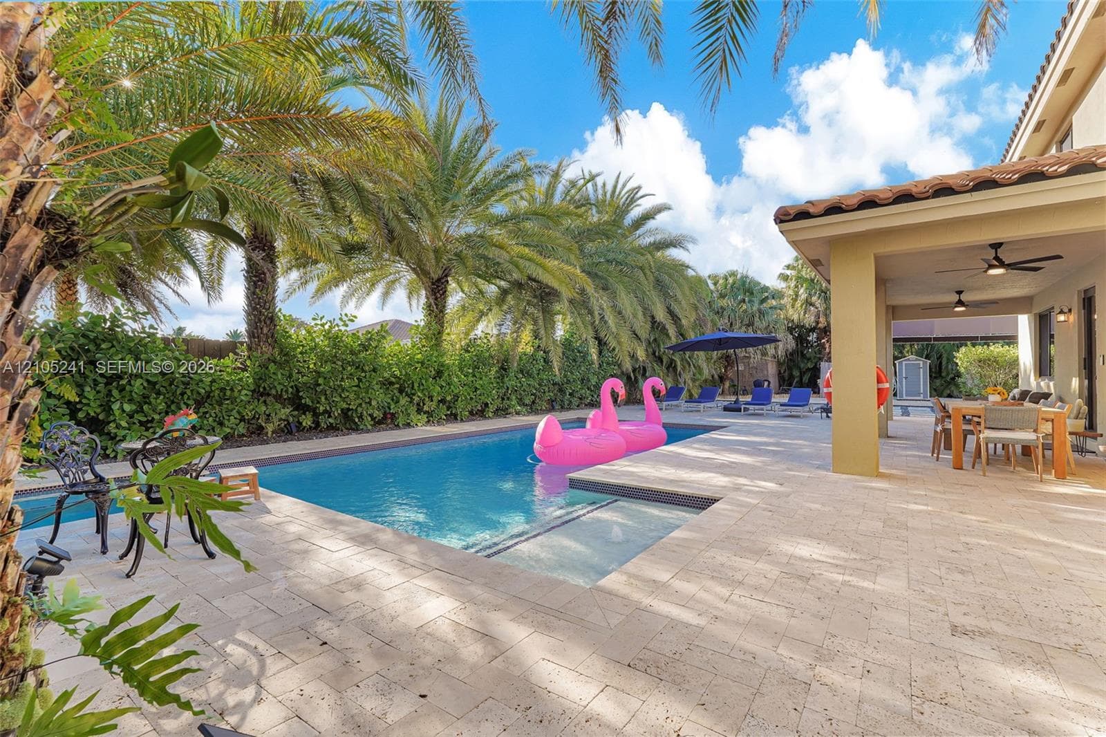 Outdoor living area featuring a swimming pool with an integrated spa, expansive paver patio, covered lanai with ceiling fans, and lush perimeter landscaping