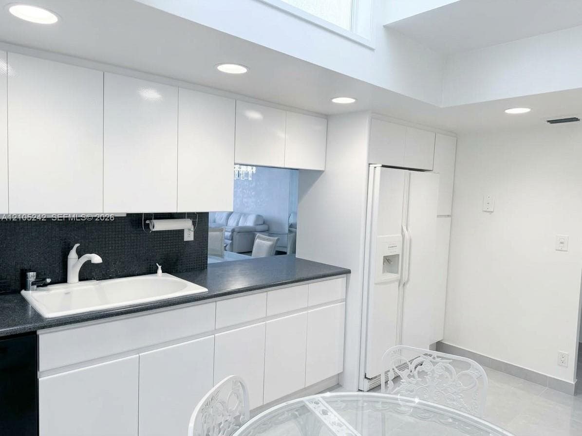 White cabinetry with integrated handles, dark countertops, a white double-basin sink, and recessed lighting