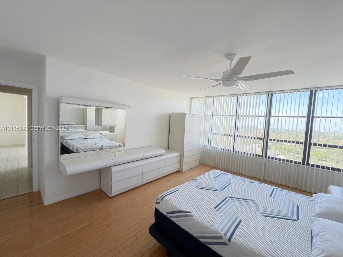 Floor-to-ceiling windows with vertical blinds, wood-finish flooring, and a ceiling fan