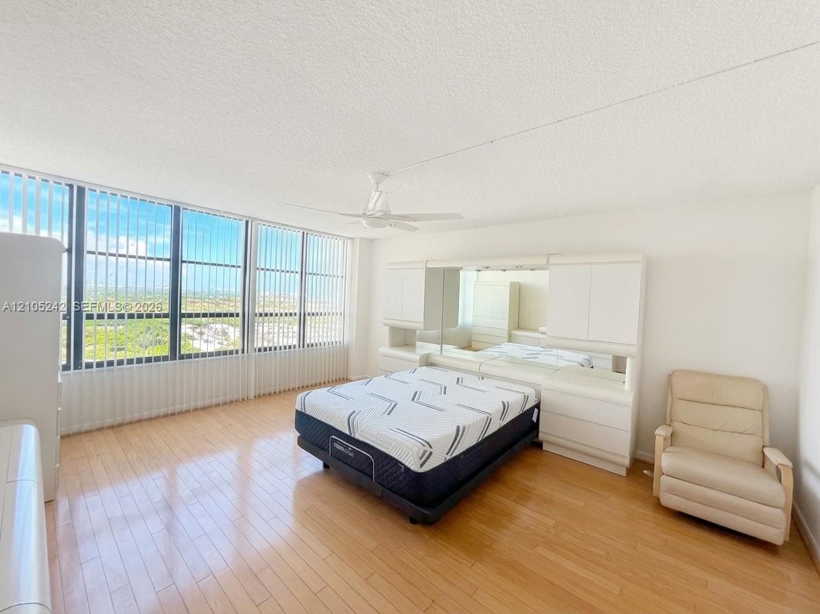 Expansive window wall with vertical blinds, light wood-finish flooring, built-in cabinetry with integrated mirrors, and a ceiling fan