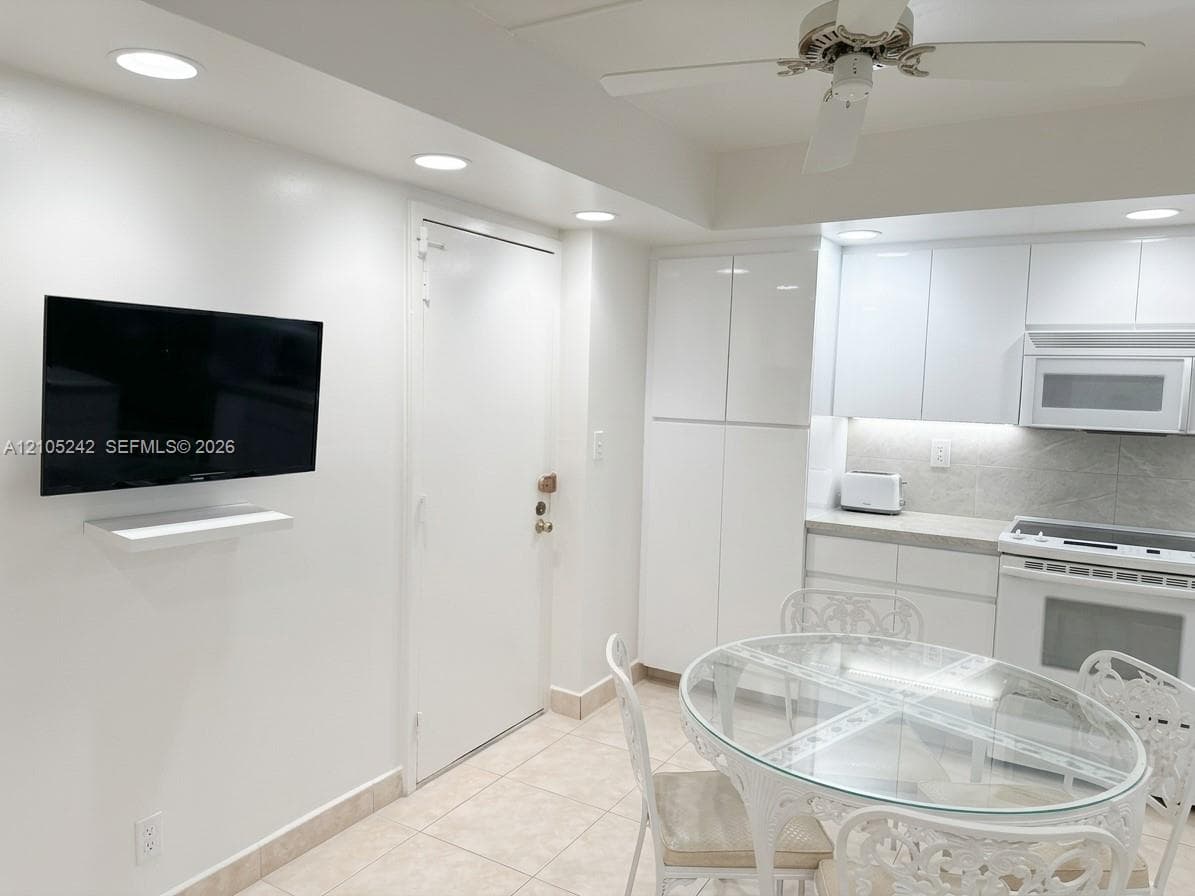 Recessed lighting, white high-gloss cabinetry, tiled flooring, integrated oven and microwave, and a ceiling fan with light fixture