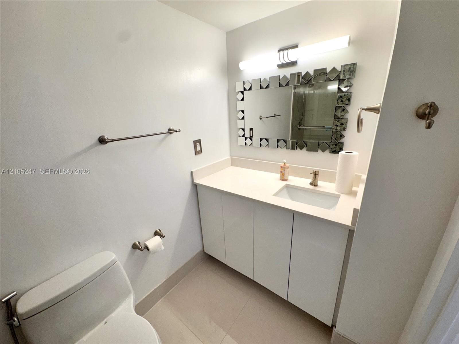 White vanity with integrated sink, contemporary mirror, and a wall-mounted light fixture