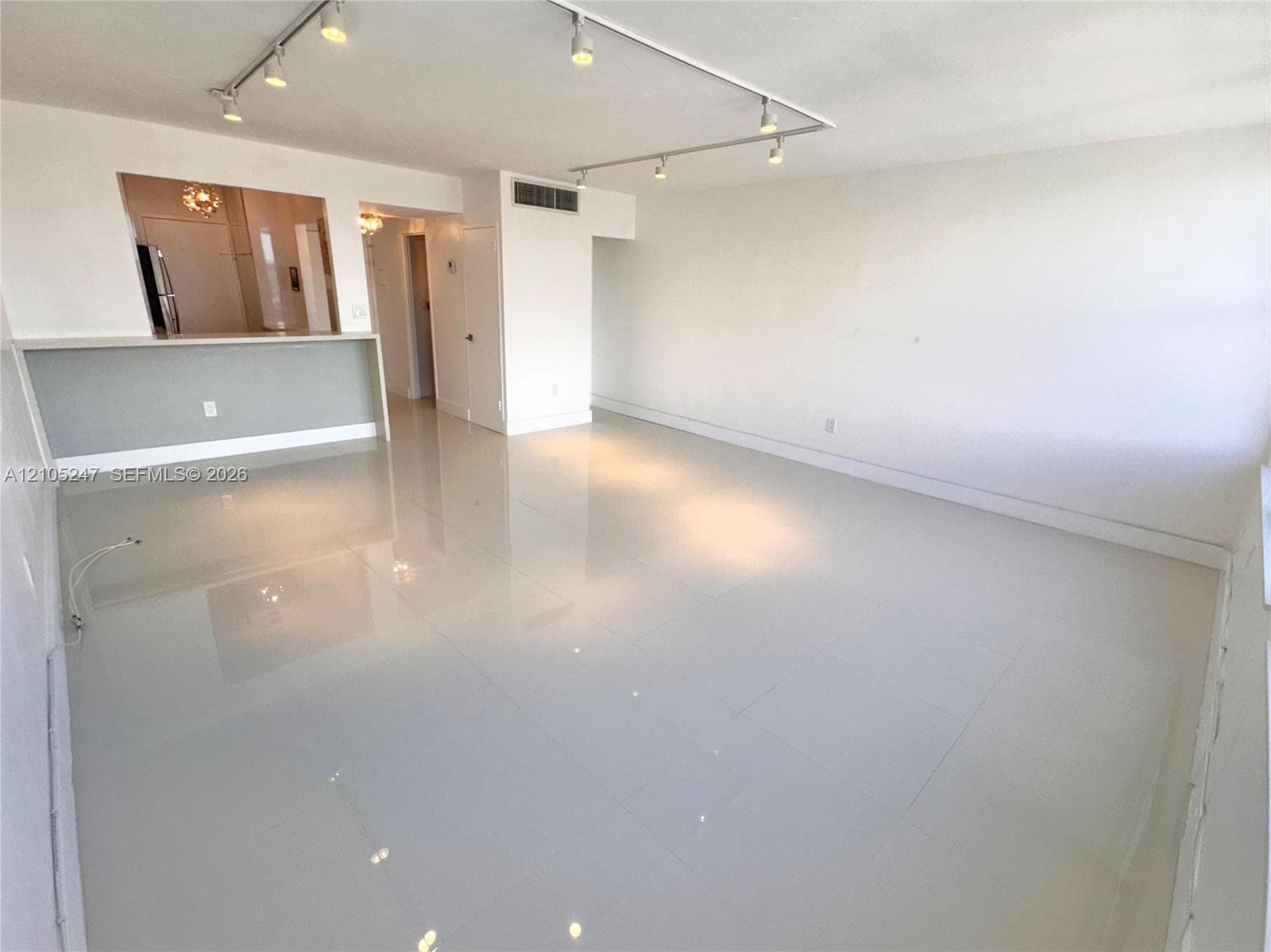 Neutral tile flooring, track lighting, and a pass-through opening to an adjacent room