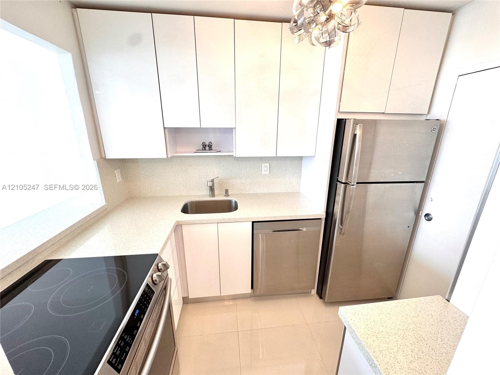 Modern kitchen featuring white flat-panel cabinetry, light-toned countertops, a stainless steel refrigerator, a stainless steel dishwasher, and a built-in range