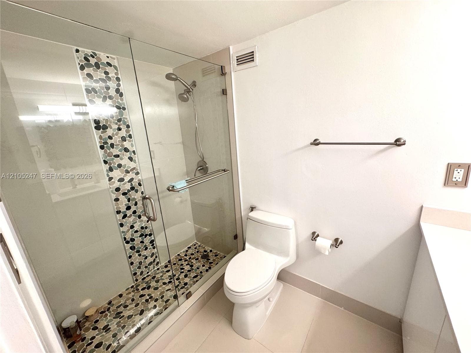 Walk-in shower with clear glass enclosure and pebble-tile accent