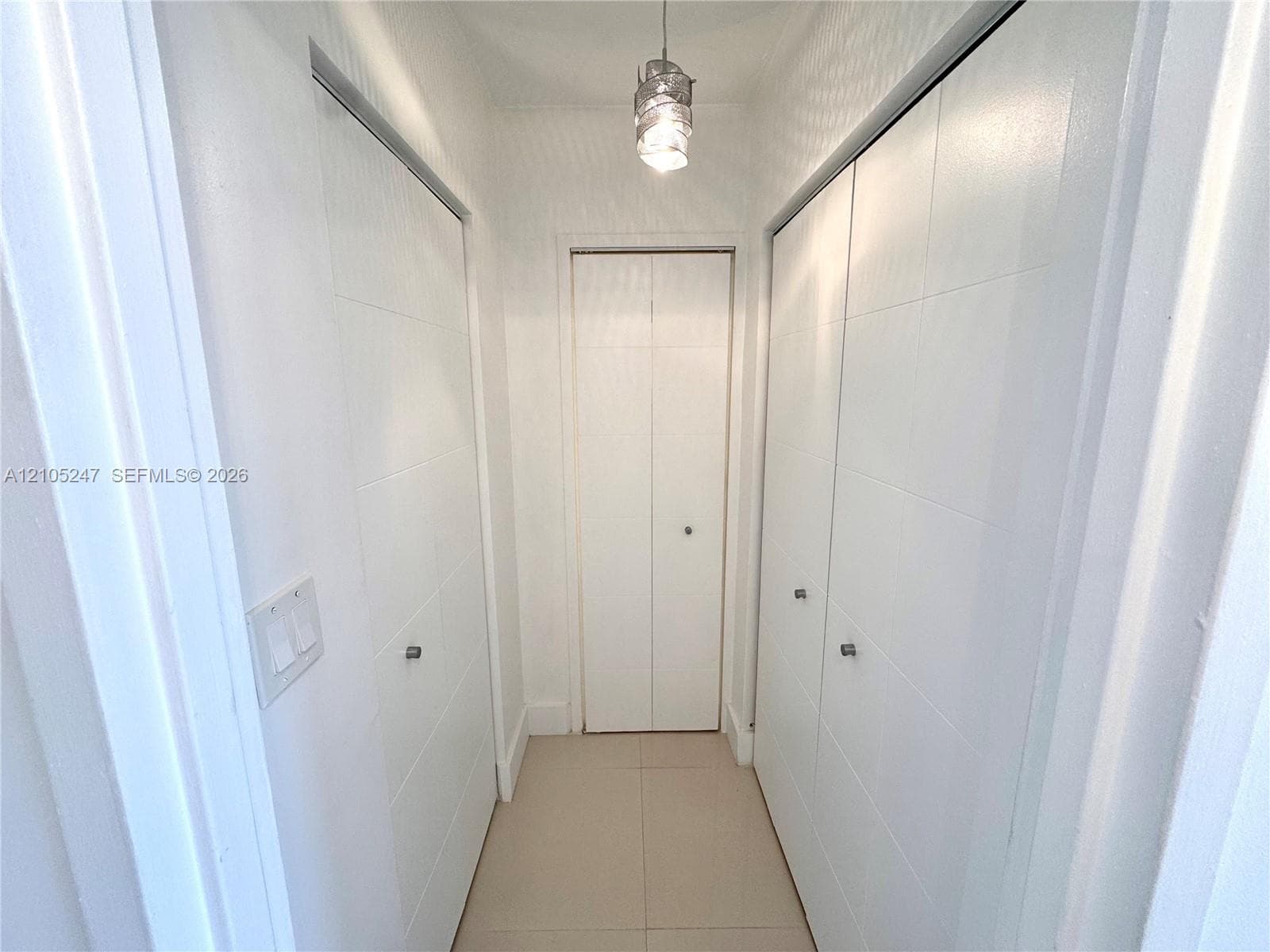 Hallway featuring multiple white paneled closet doors, recessed ceiling light fixture, and tile flooring