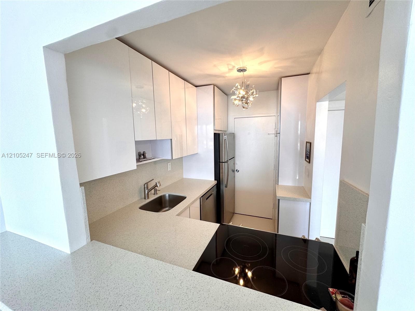 Modern kitchen featuring white glossy cabinetry, stainless steel appliances, a built-in cooktop, and light-toned countertops