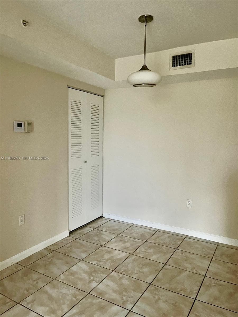 Neutral toned tile flooring, louvered bi-fold closet door, and a suspended ceiling light fixture