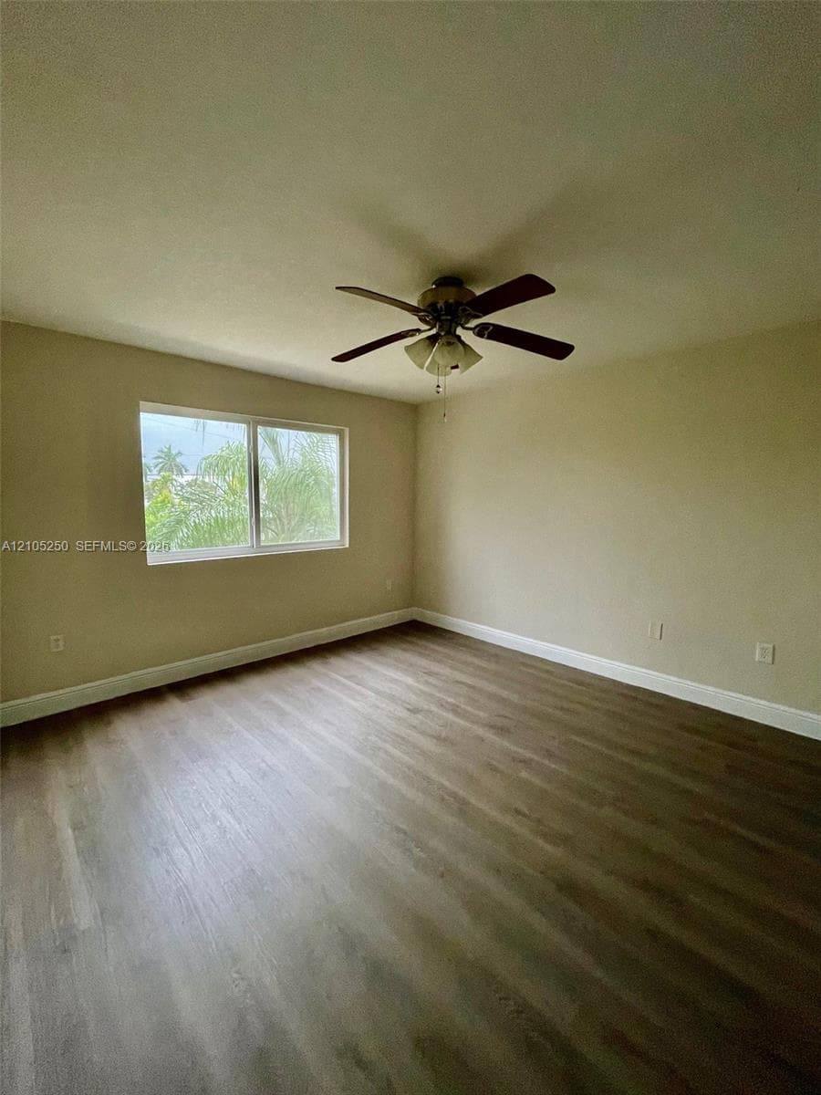 Spacious room featuring wood-finish flooring, a ceiling fan with integrated lighting, and a large window