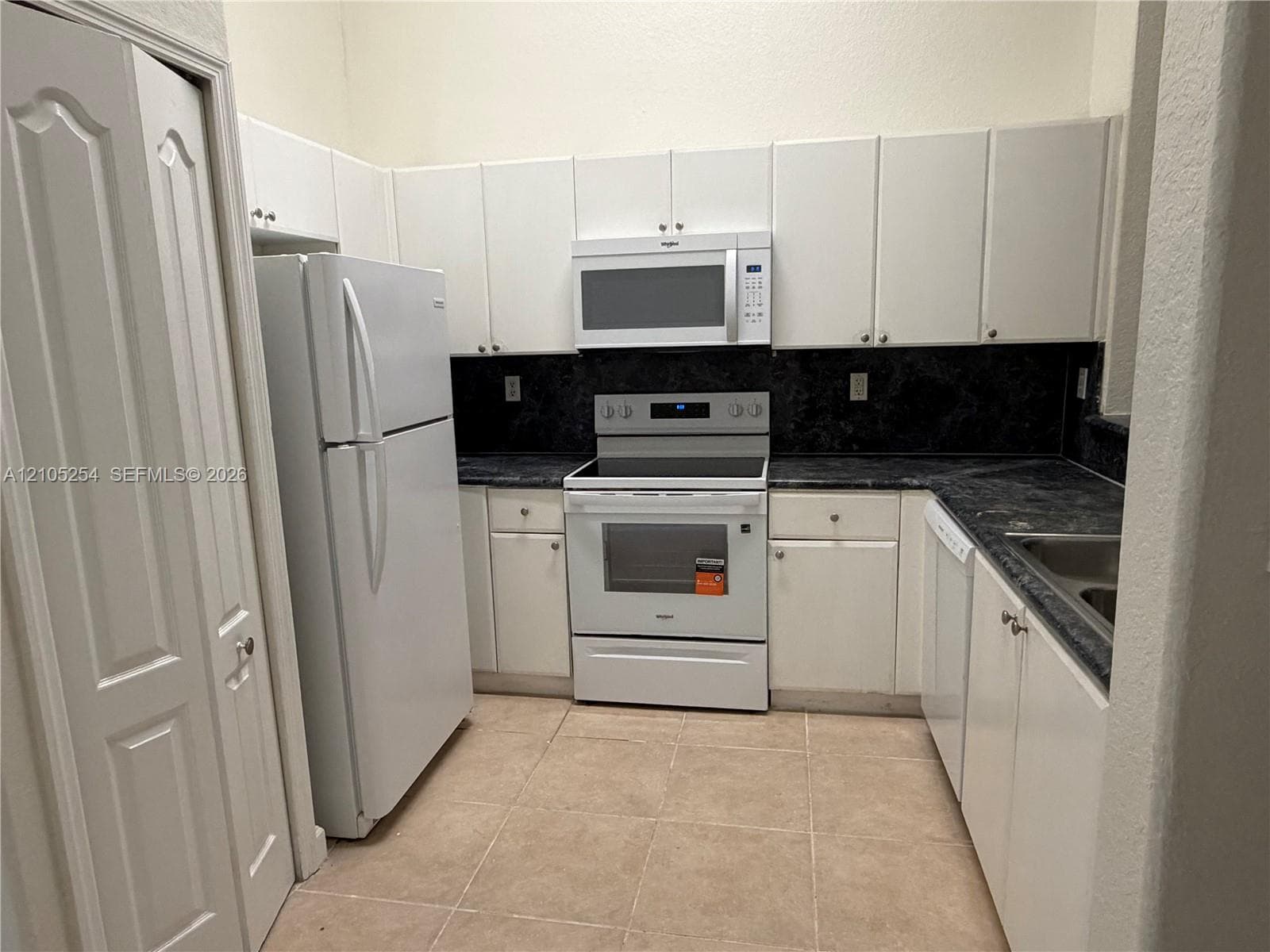 Kitchen featuring white cabinetry, dark countertops, white refrigerator, and a white range with an above-range microwave