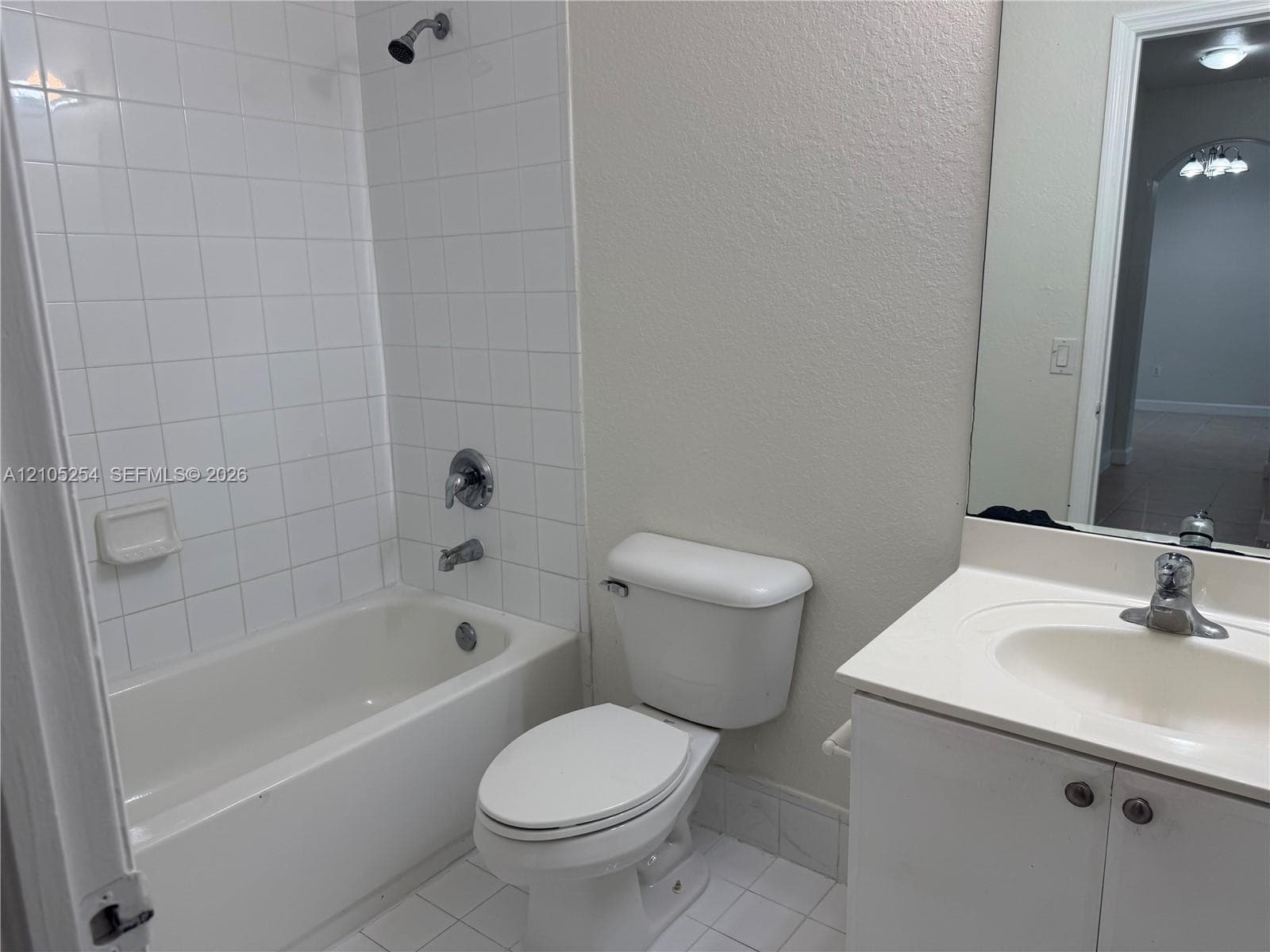 White tiled flooring with a built-in bathtub, shower with chrome fixtures, and a white vanity with an integrated sink