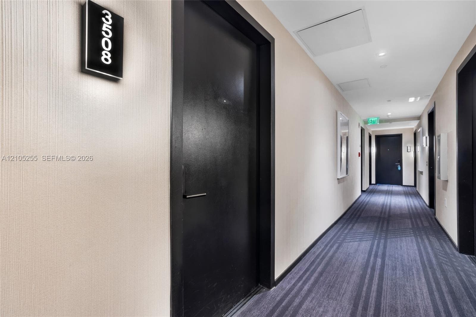 Hallway featuring textured wall coverings, dark-finished entry doors, recessed ceiling lighting, and striped pattern carpeting