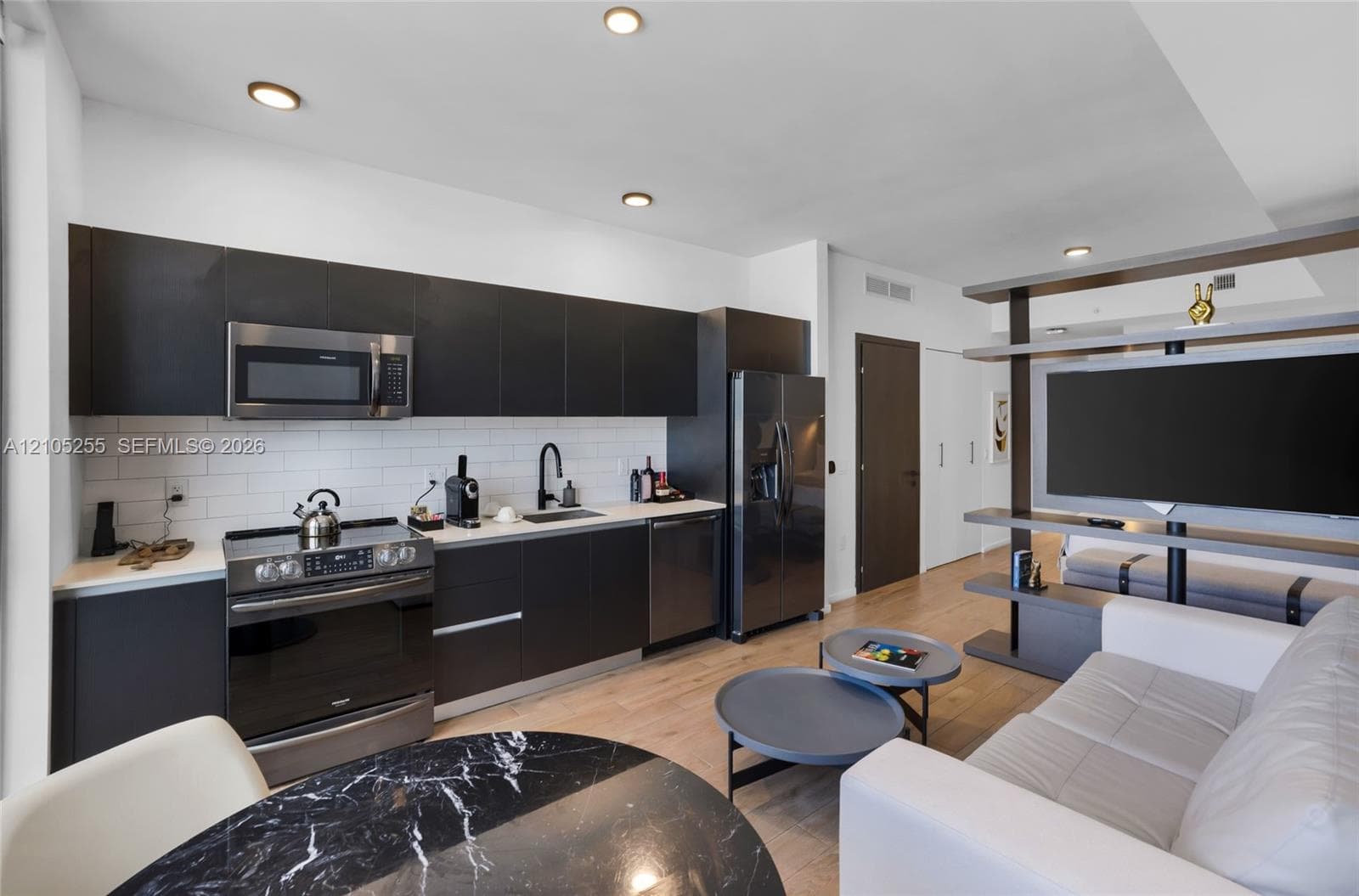 Kitchen featuring matte dark cabinetry, white subway tile backsplash, light wood-finish flooring, recessed lighting, and stainless steel appliances