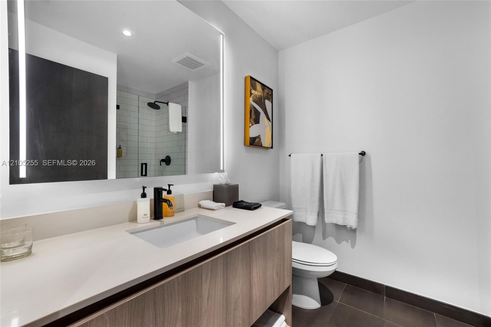 Floating wood-finish vanity with integrated rectangular basin, quartz countertop, illuminated wall-mounted mirror, and walk-in shower with matte black fixtures