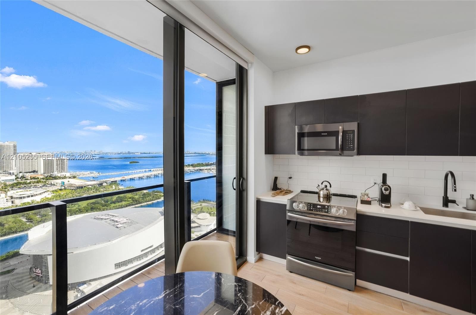 Kitchen featuring flat-panel cabinetry, light-toned countertops, white subway tile backsplash, stainless steel appliances, and floor-to-ceiling glass sliding doors with water and city skyline outlook