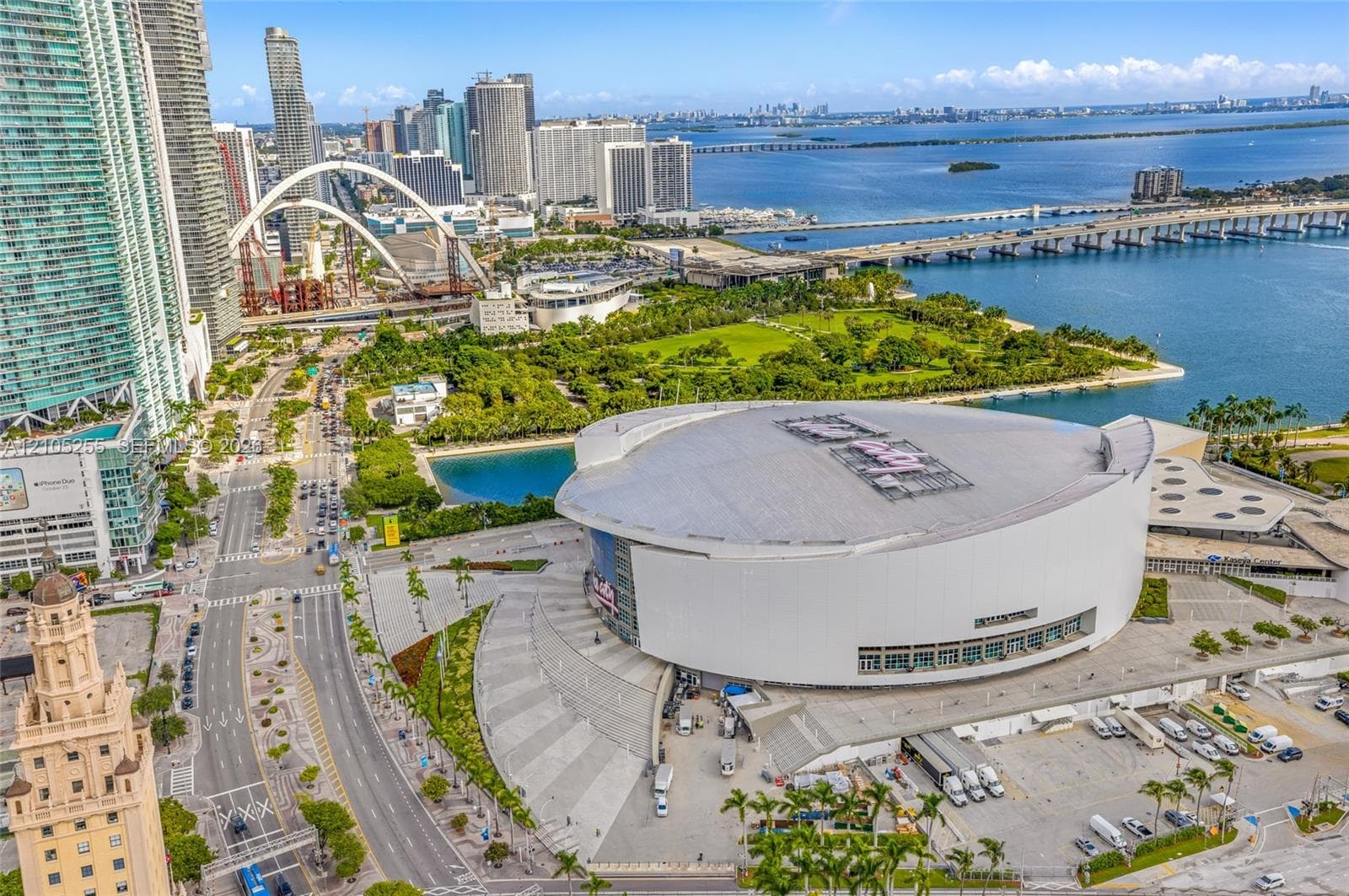 Aerial perspective of the metropolitan waterfront featuring a prominent circular arena, expansive paved public plaza, proximity to bayfront parkland, and surrounding high-rise urban infrastructure