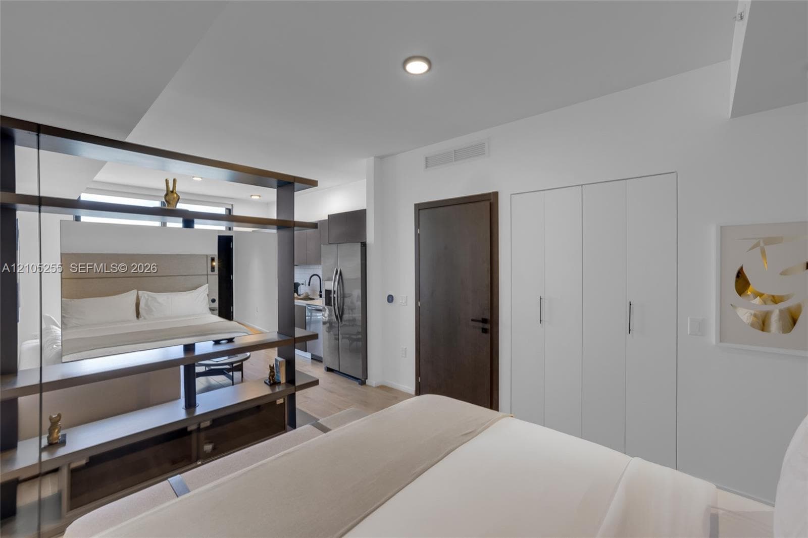 Open-concept interior featuring wood-finish flooring, a built-in dark-toned partition with integrated shelving, white bi-fold closet doors, and recessed lighting