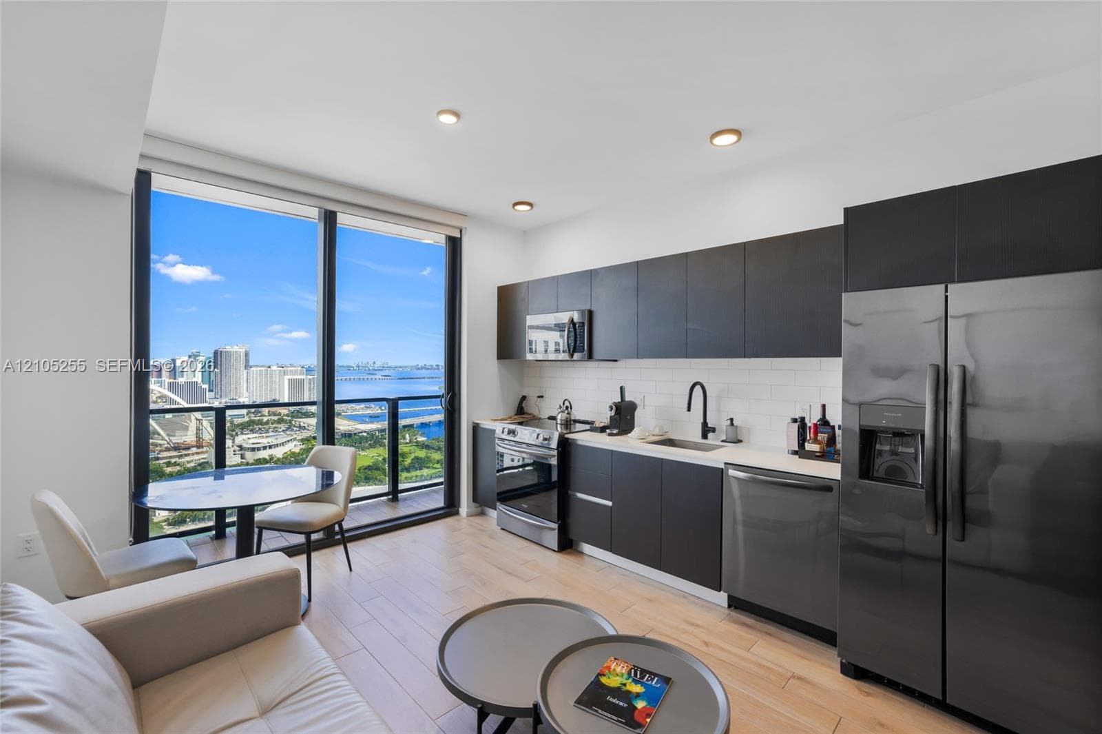 Kitchen featuring dark flat-panel cabinetry, light countertops, subway tile backsplash, stainless steel appliances, and wood-finish flooring with floor-to-ceiling windows