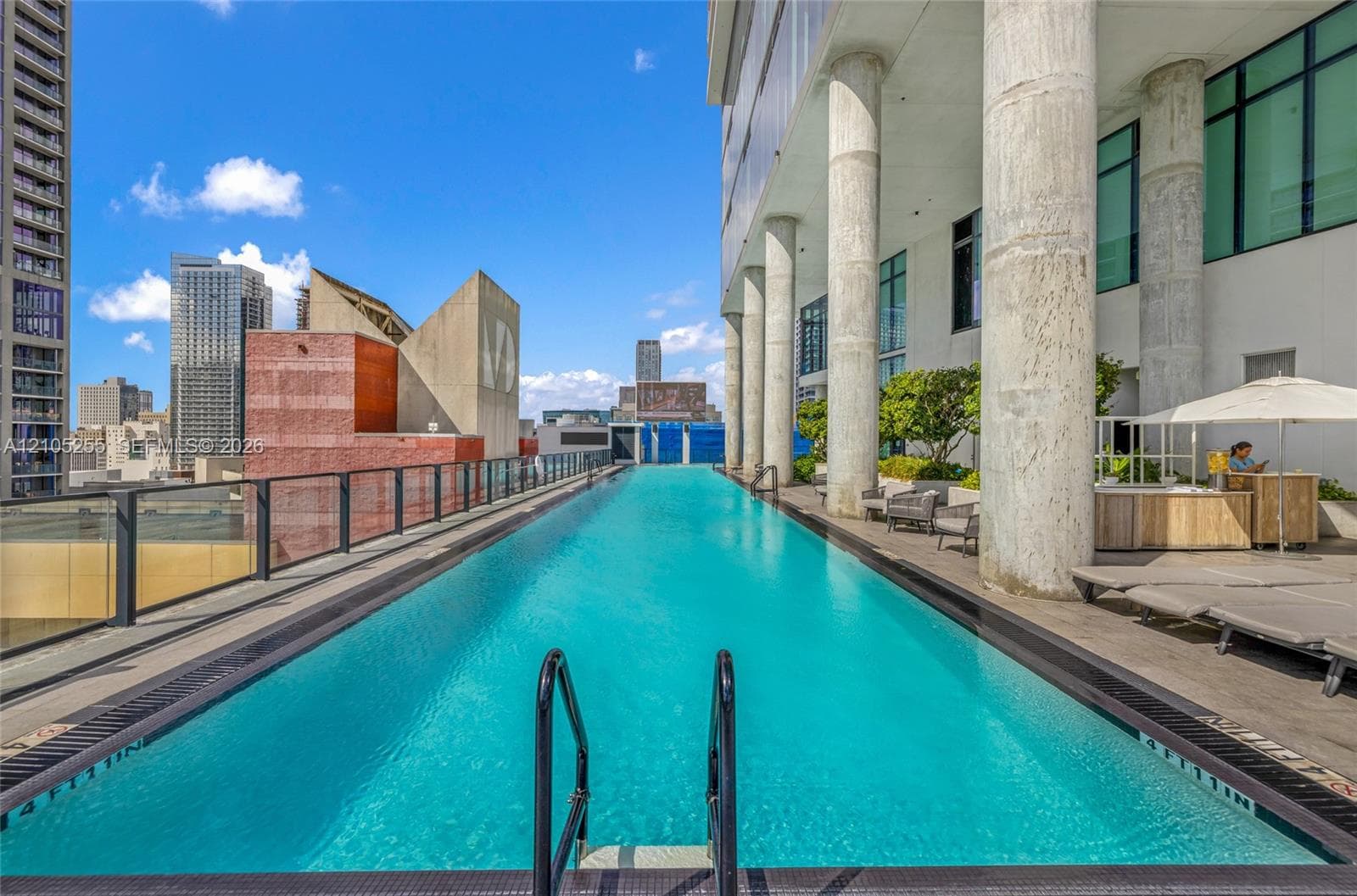 Lap pool with tile perimeter, structural concrete columns, and glass panel railing