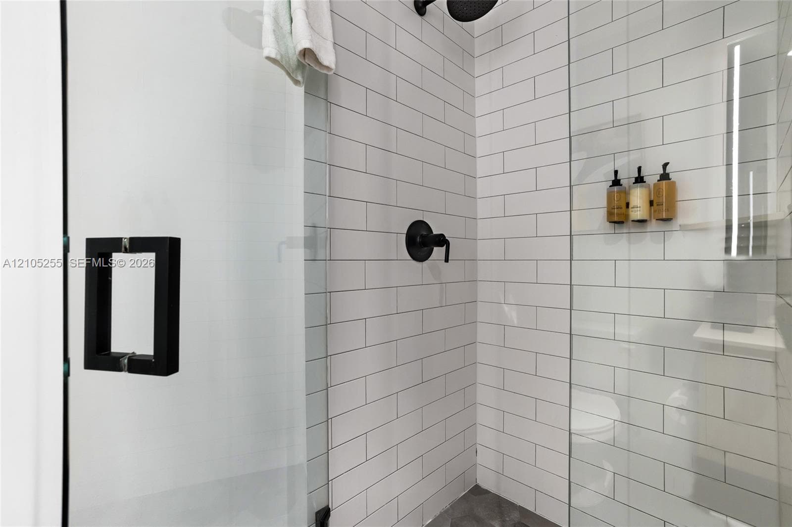 Walk-in shower featuring white subway wall tile, glass enclosure with matte black hardware, integrated storage niche, and matte black plumbing fixtures
