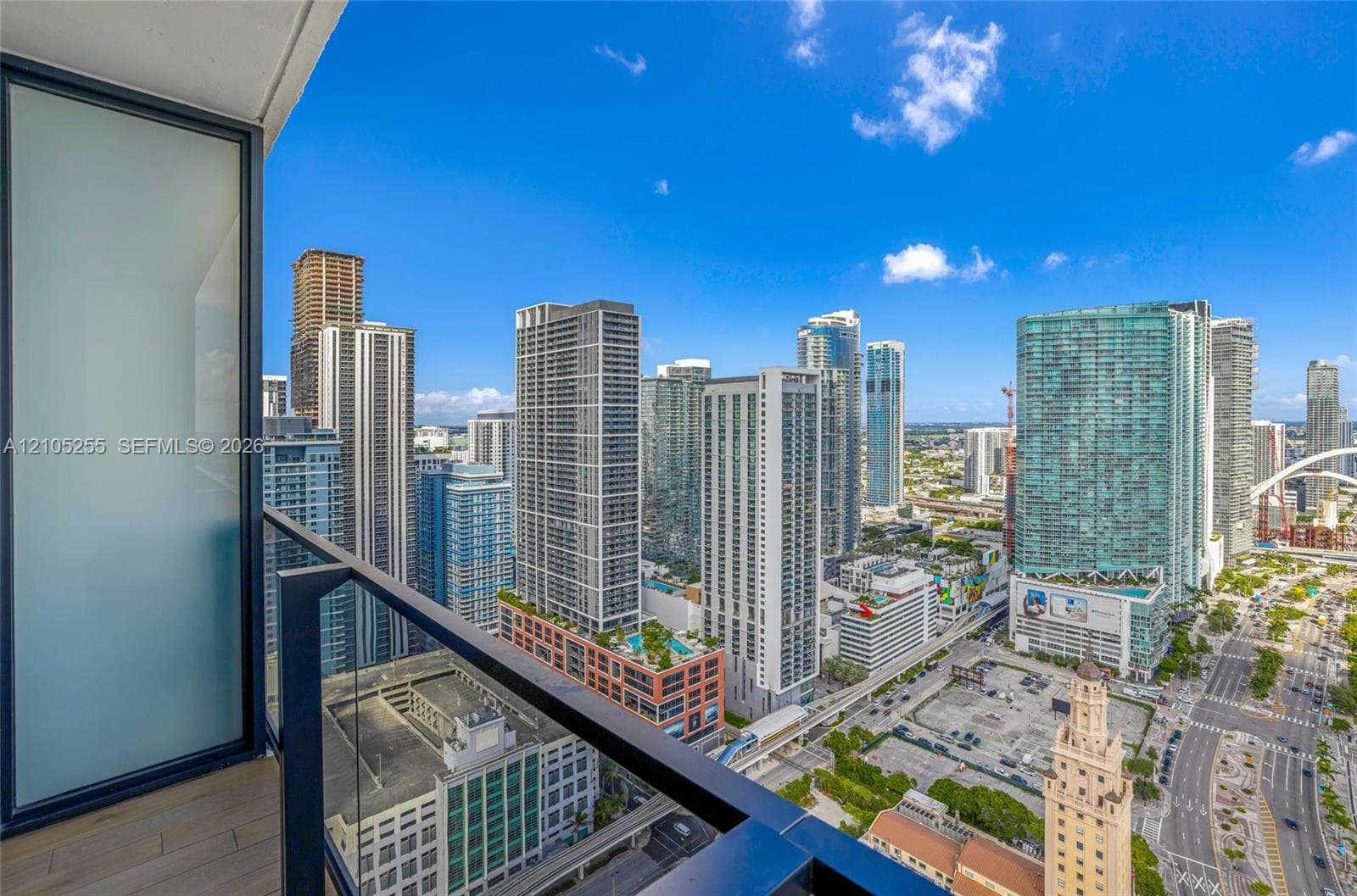 Private balcony featuring glass panel railings, frosted glass privacy screen, and urban skyline panorama