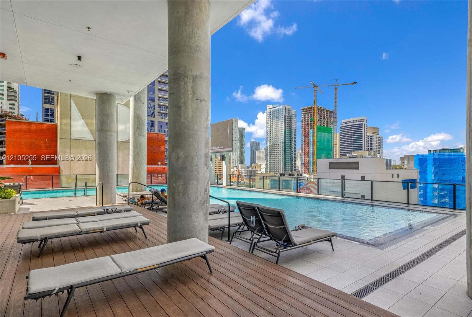 Rooftop swimming pool with tile surround, wood-finish deck, concrete structural columns, and glass panel railing