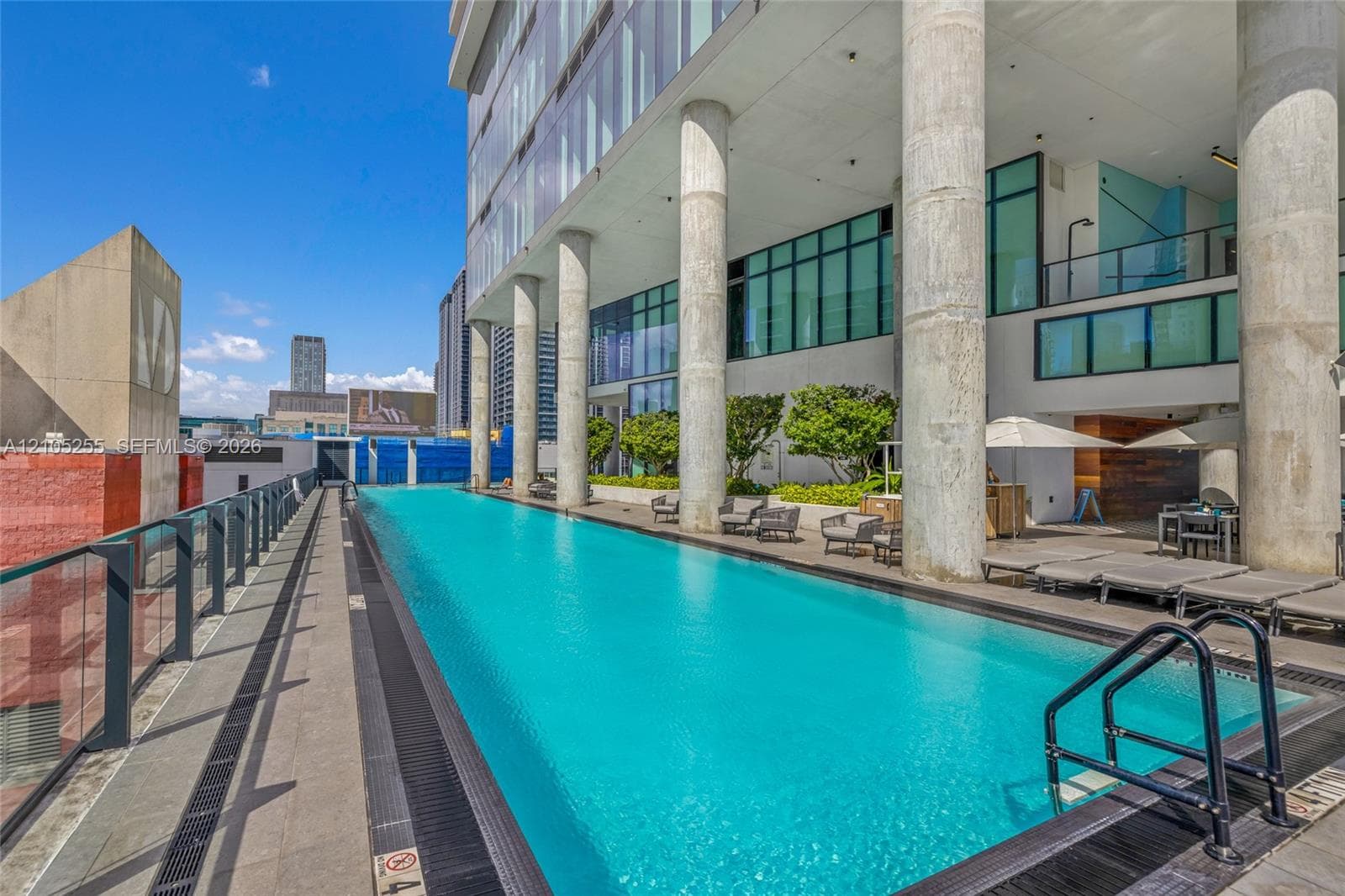 Elevated lap pool featuring glass perimeter railings, concrete structural pillars, and concrete terrace decking