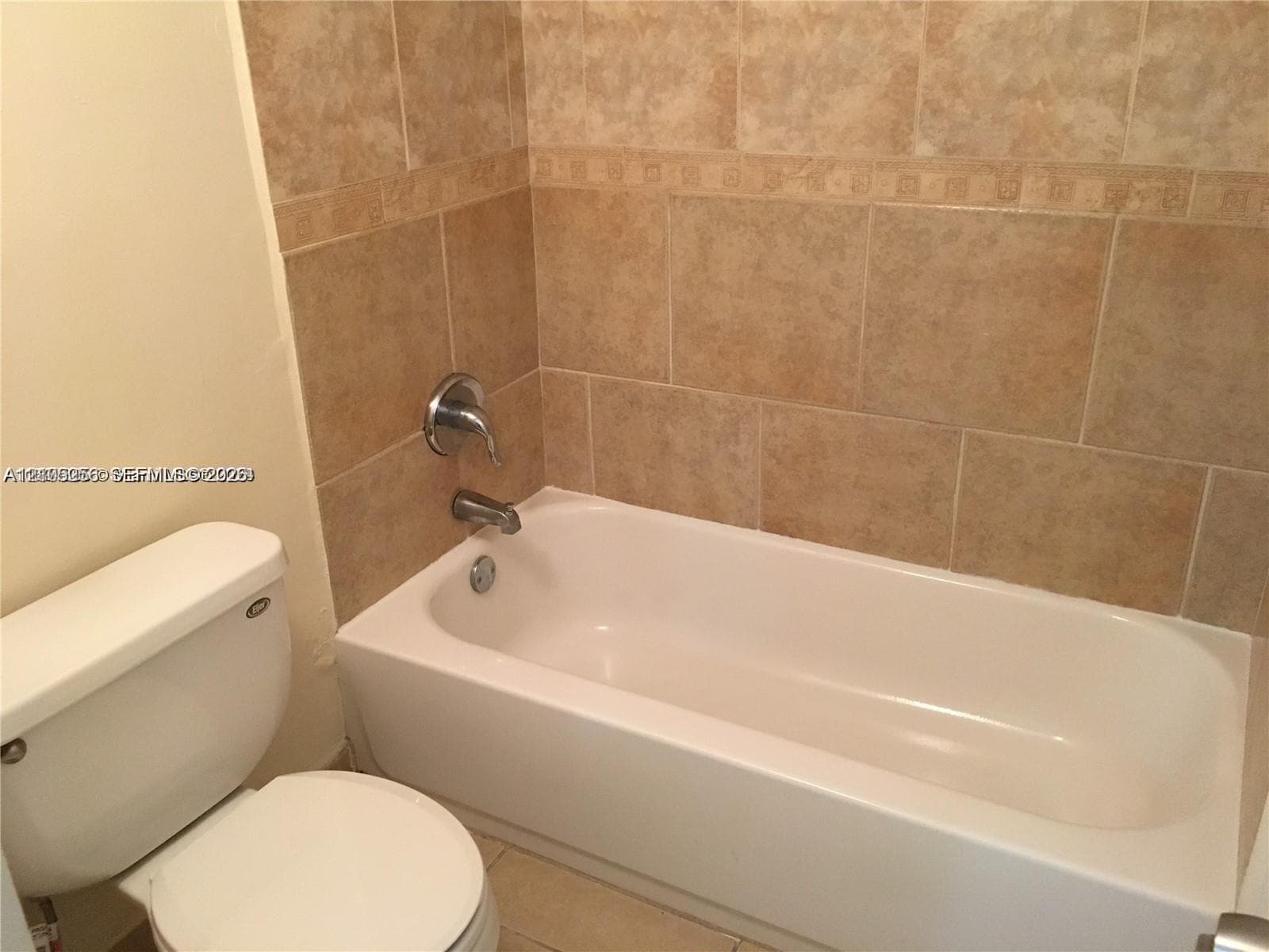 Full-size bathtub with integrated shower faucet and surround wall featuring neutral stone-finish ceramic tile with decorative accent banding