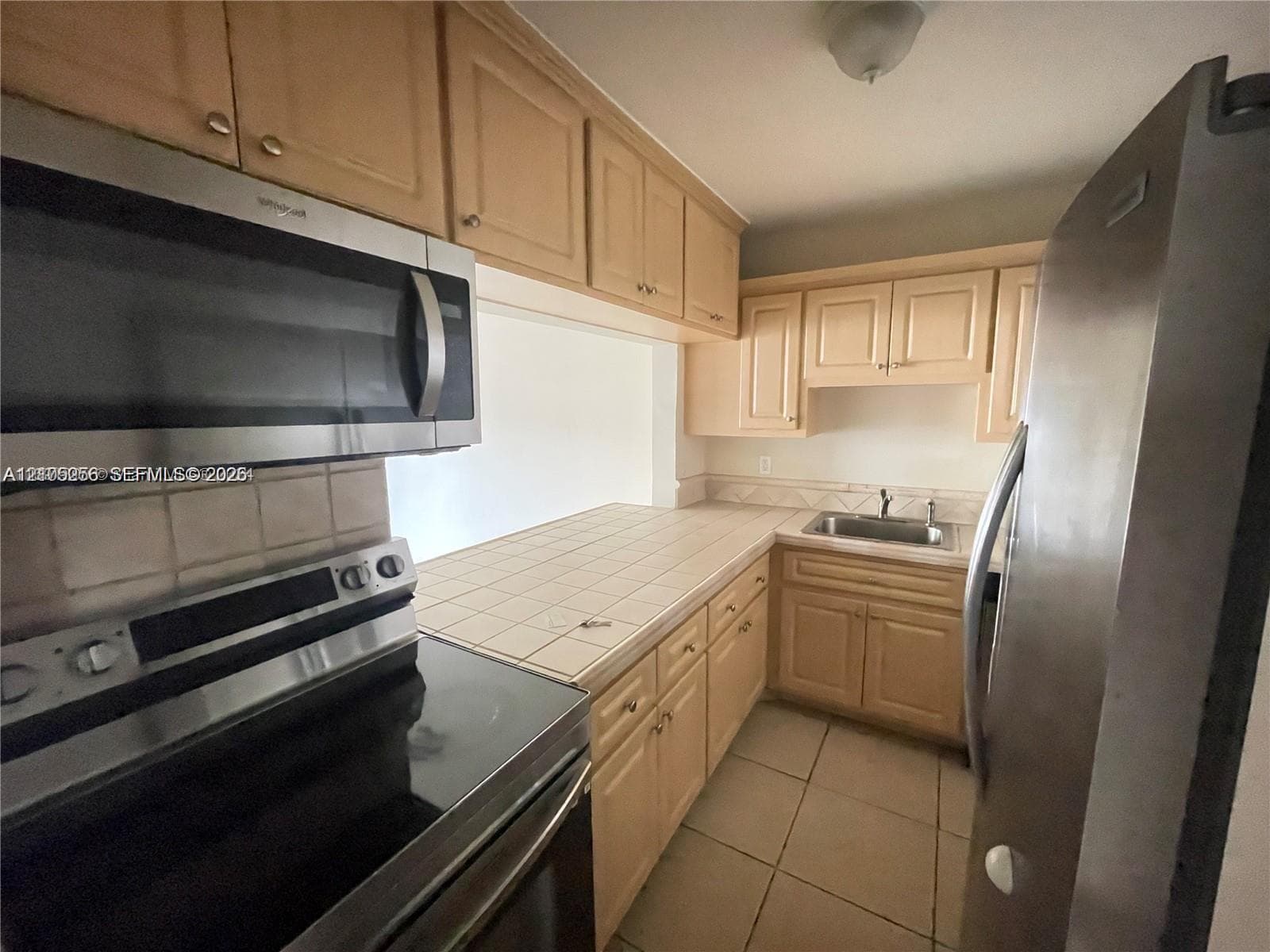 Kitchen featuring light wood-finish cabinetry, tile countertops, stainless steel appliances, and tile flooring