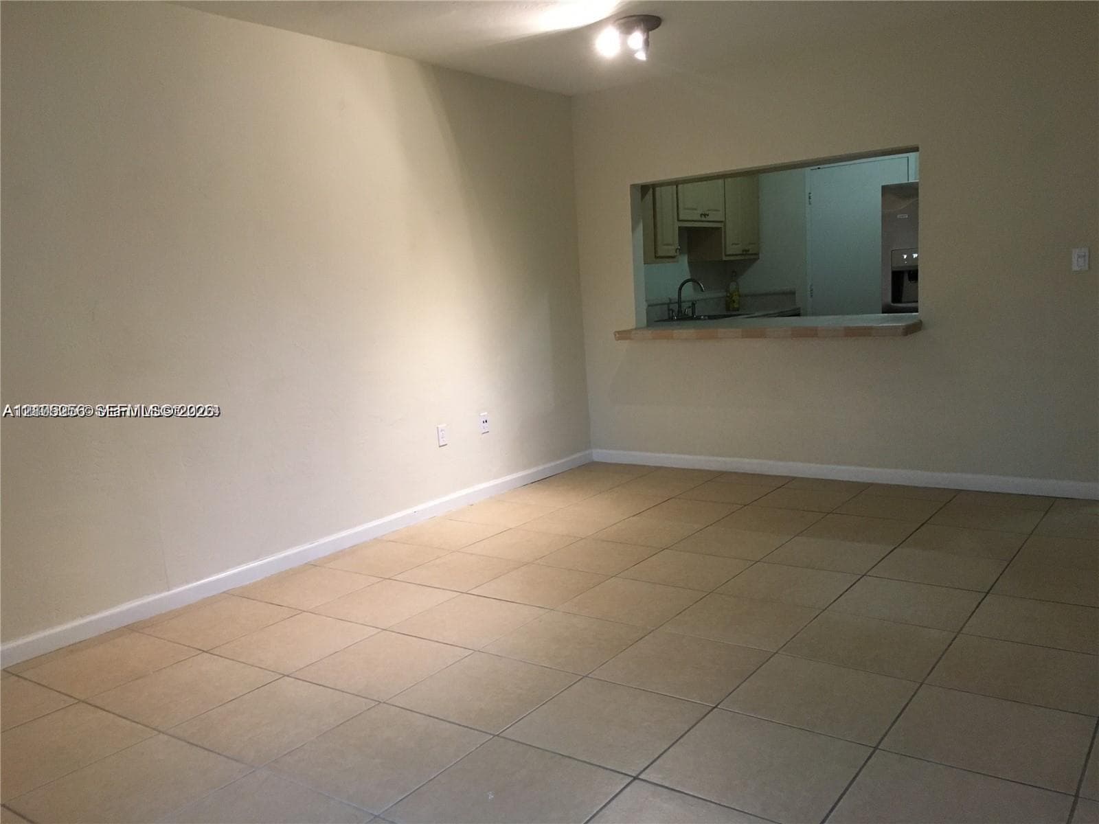 Neutral tile flooring, pass-through opening to kitchen, countertop ledge, and ceiling-mounted dual-bulb light fixture