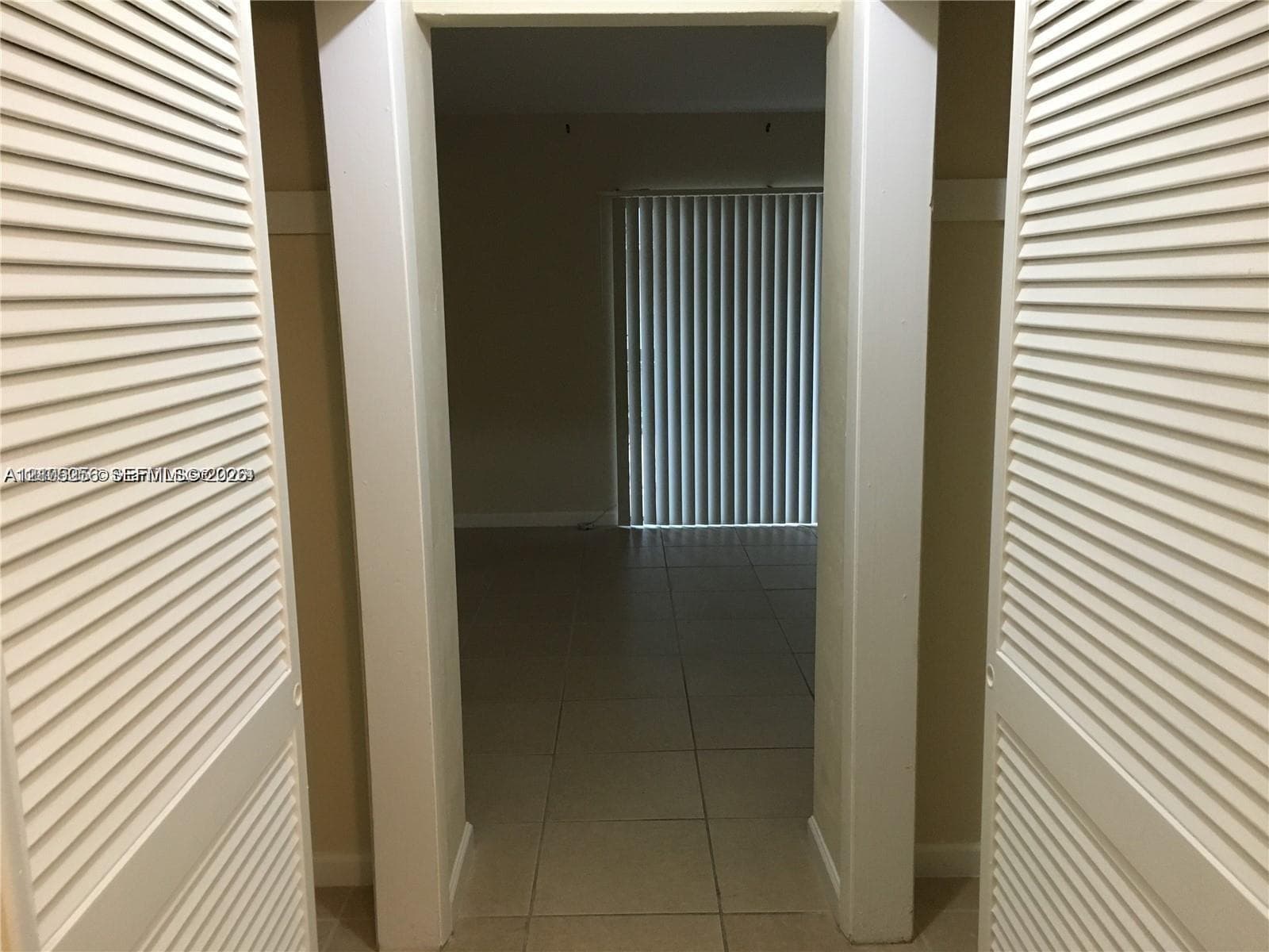 Double louvered closet doors with ceramic tile flooring and floor-to-ceiling vertical window blinds