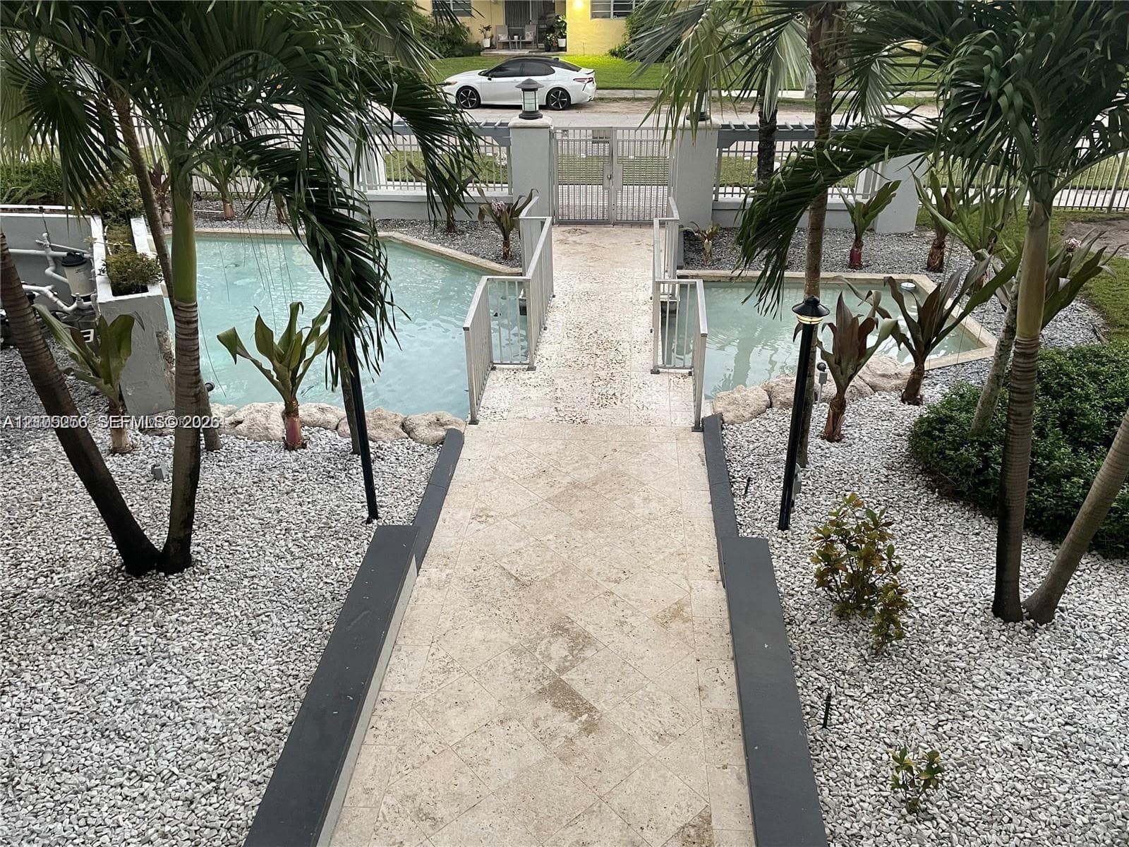 Split-level pool area featuring a stone-paved walkway, rock-bordered aquatic features, metal fencing, and integrated landscape lighting