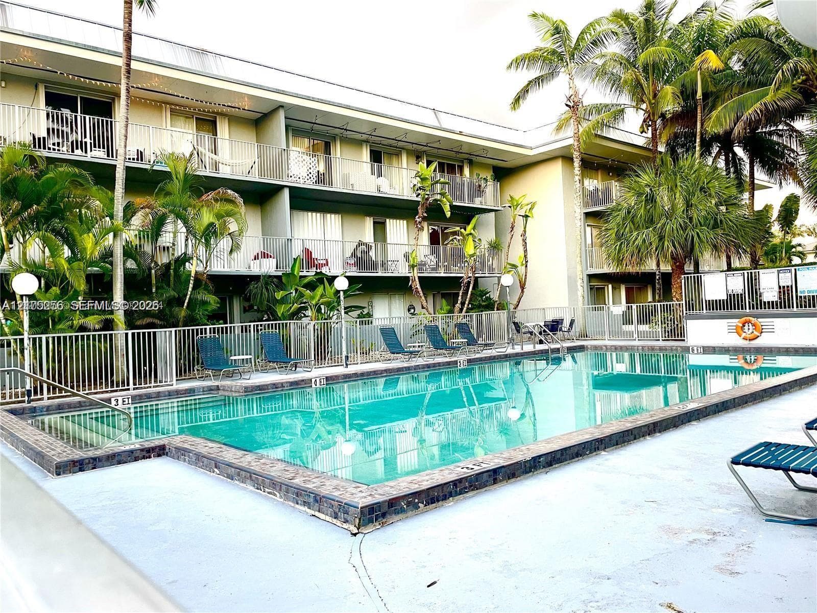 Swimming pool with tile surround, metal perimeter fencing, multi-level balconies, and mature palm trees