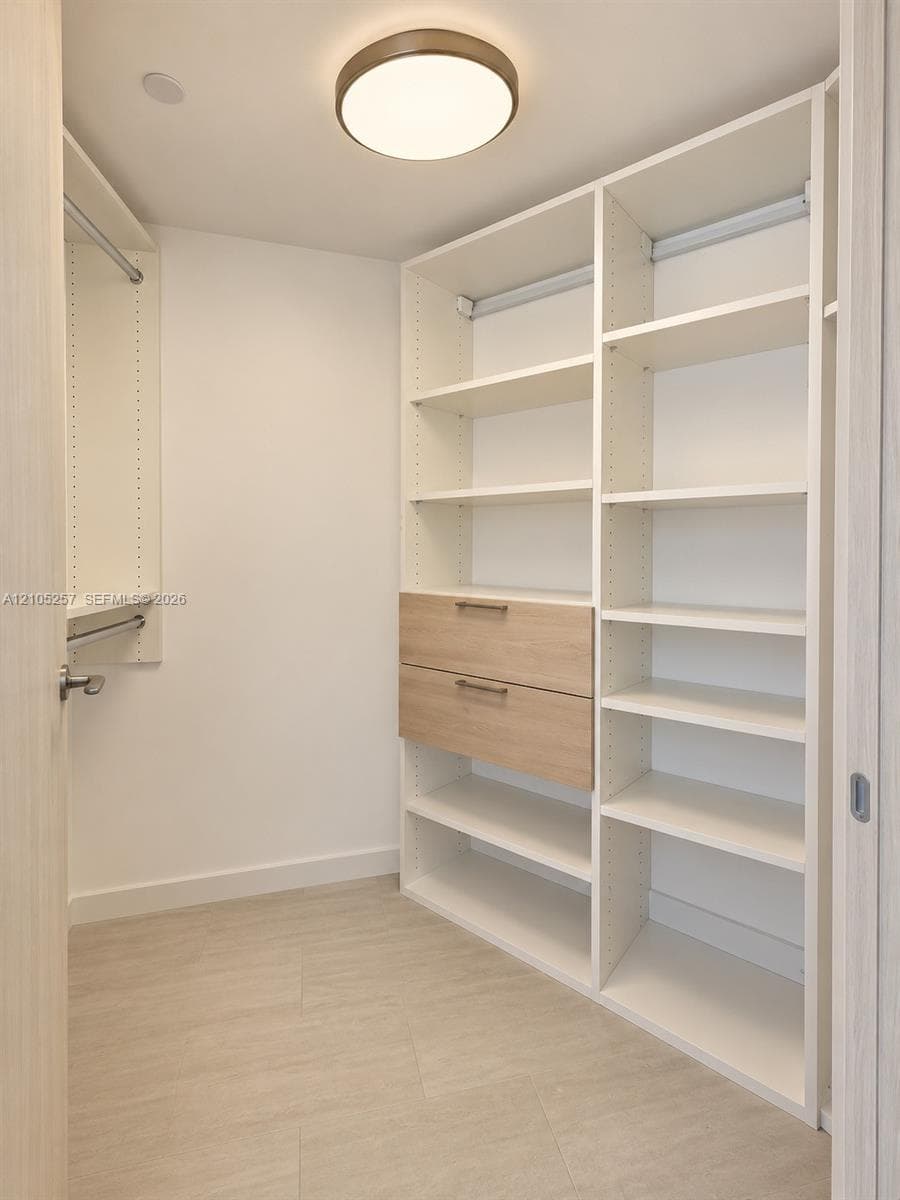Custom storage closet featuring adjustable shelving, integrated drawers with metallic pulls, dual hanging rods, and a flush-mount circular overhead light fixture