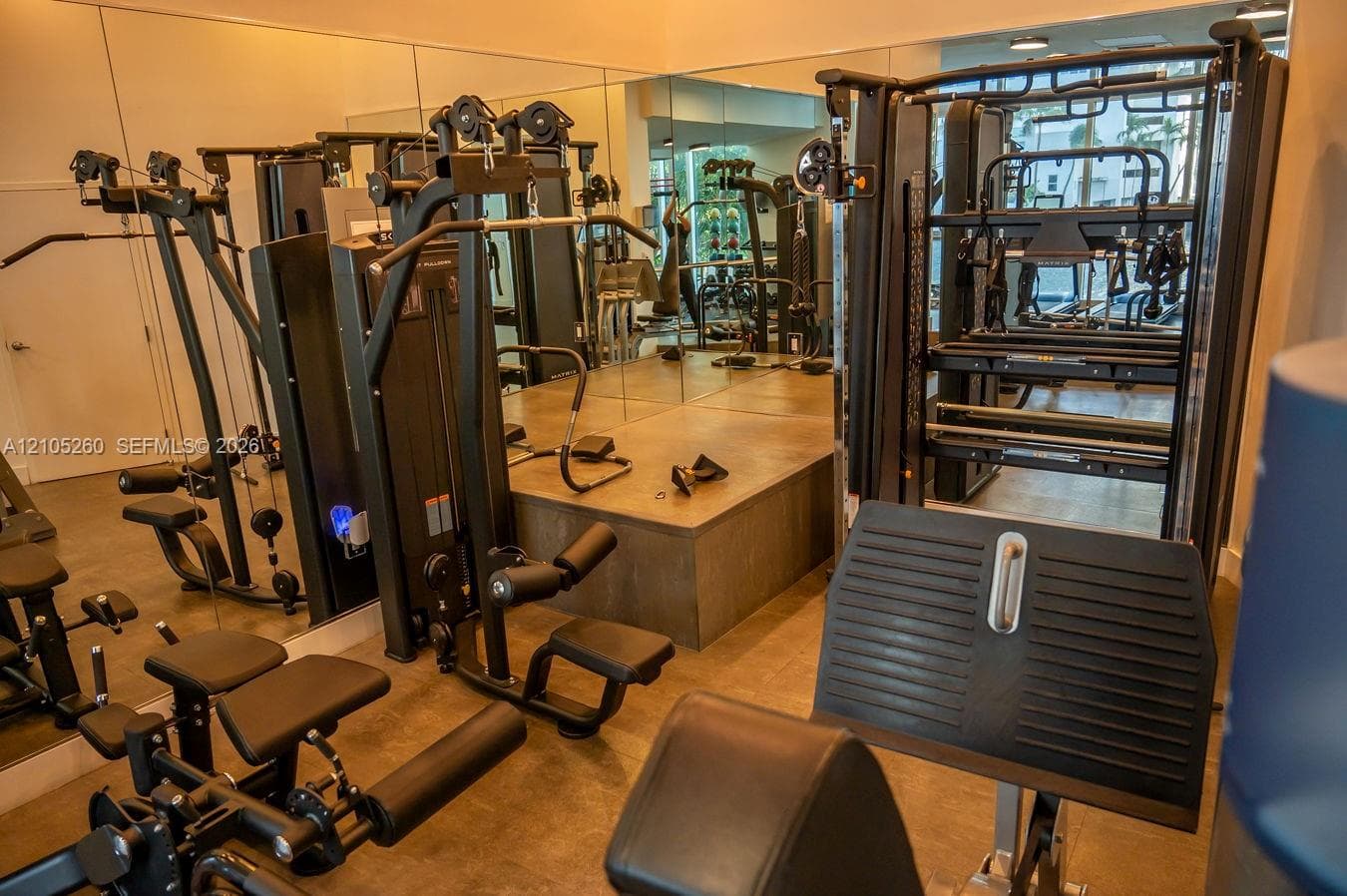 Dedicated fitness area featuring extensive mirrored walls, multiple exercise machines, and a raised platform