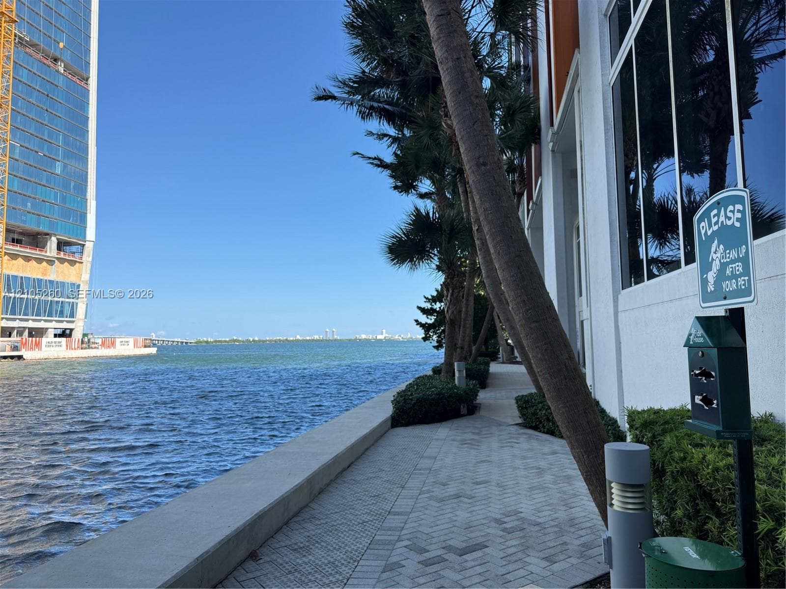 Waterfront paver walkway featuring floor-to-ceiling glass windows, integrated landscape lighting, mature palm trees, and manicured shrubbery
