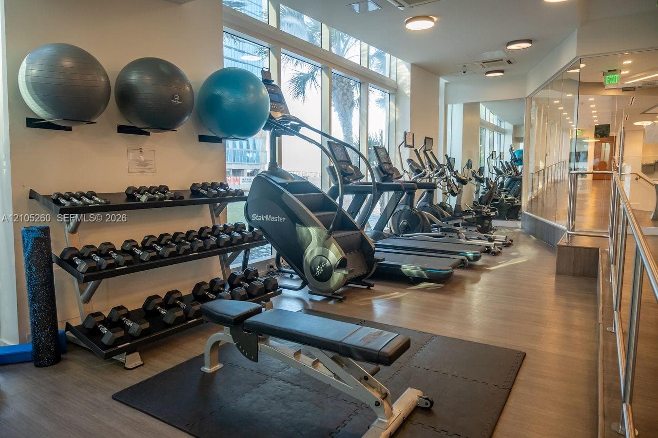 Fitness area featuring high ceilings, extensive window-walls, built-in dumbbell racks, and exercise equipment