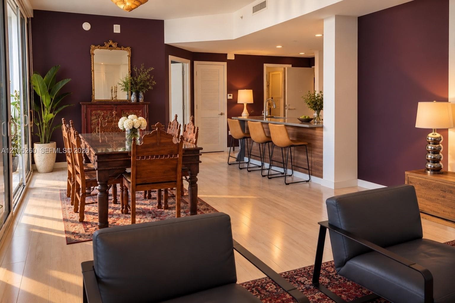 Open-concept living space featuring wood-finish flooring, deep-toned accent walls, recessed lighting, and a kitchen island with a stone countertop and breakfast bar seating