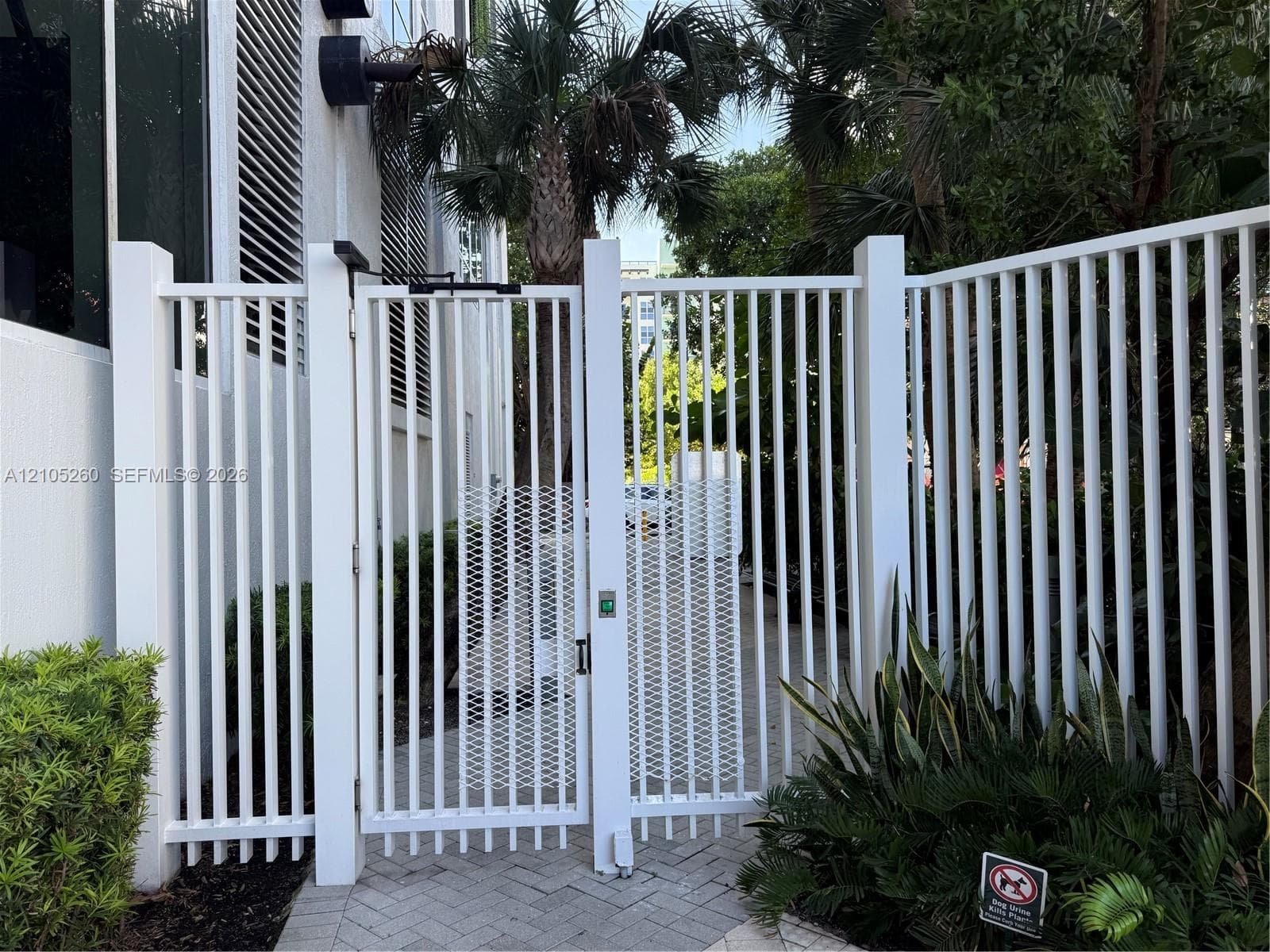 White vertical picket fencing featuring a secure metal gate with integrated electronic access panel and paver stone walkway