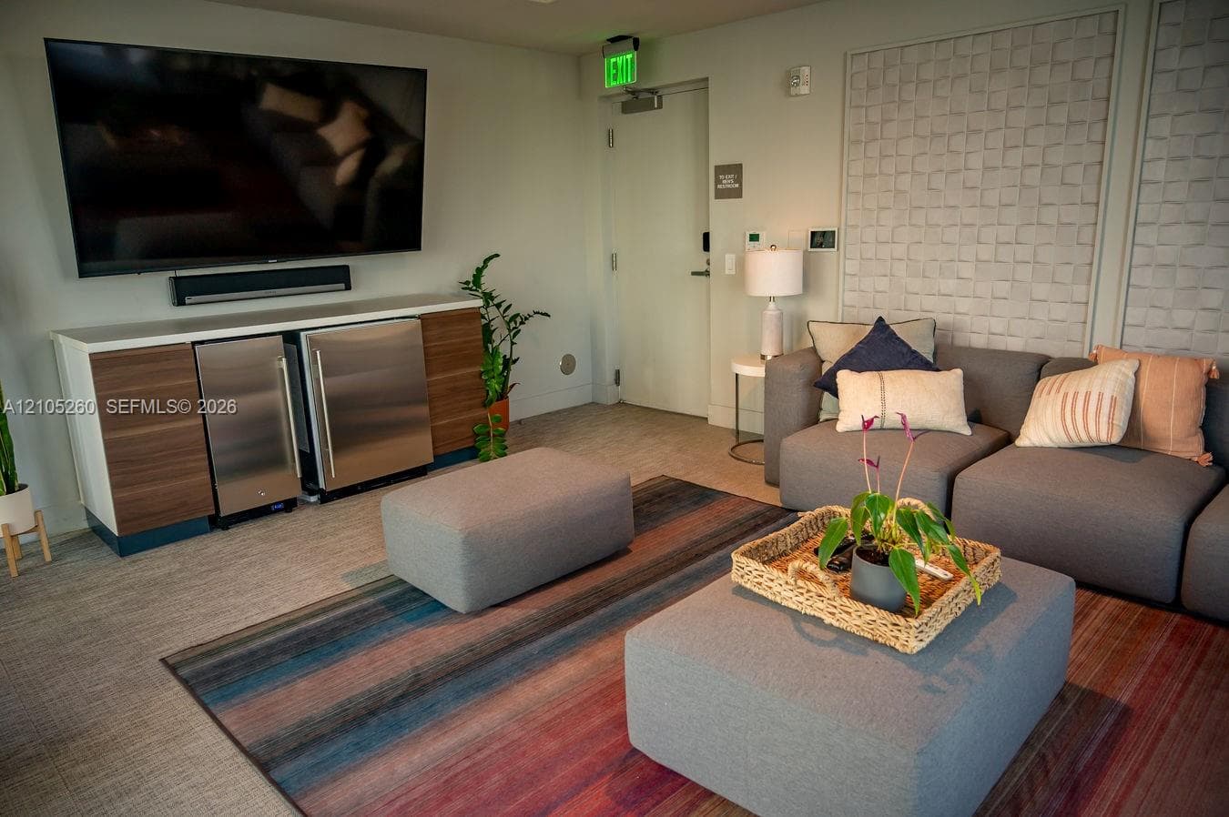 Wall-mounted television with soundbar, built-in cabinetry featuring wood-finish doors and stainless steel beverage refrigerators, and textured wall panels
