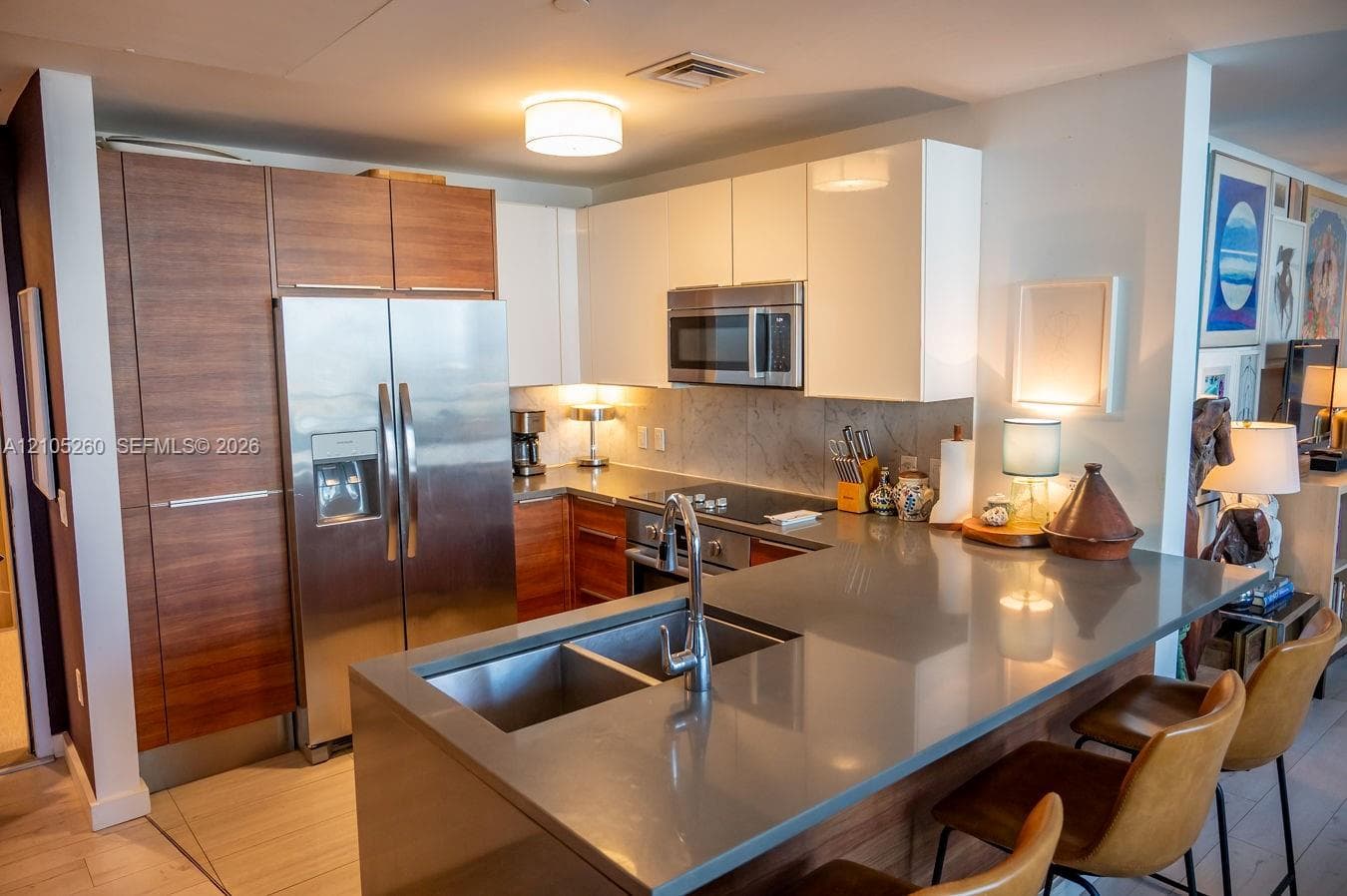 Integrated kitchen featuring wood-finish and white cabinetry, stainless steel appliances, a dual basin undermount sink, and a peninsula with a stone countertop