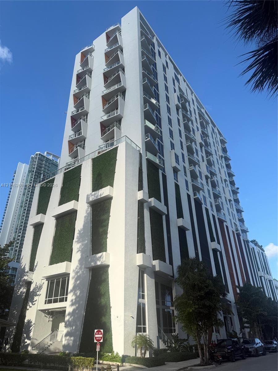 Contemporary high-rise architecture featuring multiple balconies, a green wall facade, and street-level landscaping