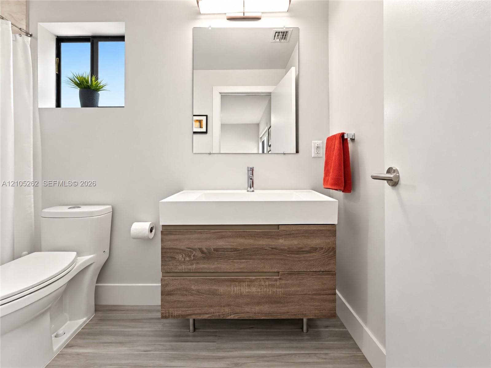 Floating wood-finish vanity with an integrated sink, polished chrome faucet, and rectangular mirror